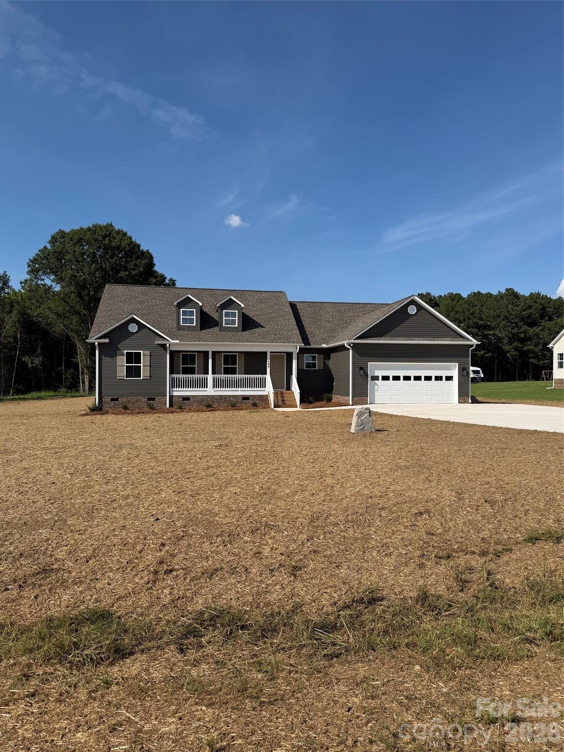 Dark gray house with white trim, two dormers, a covered porch, and an attached garage on a cleared lot.