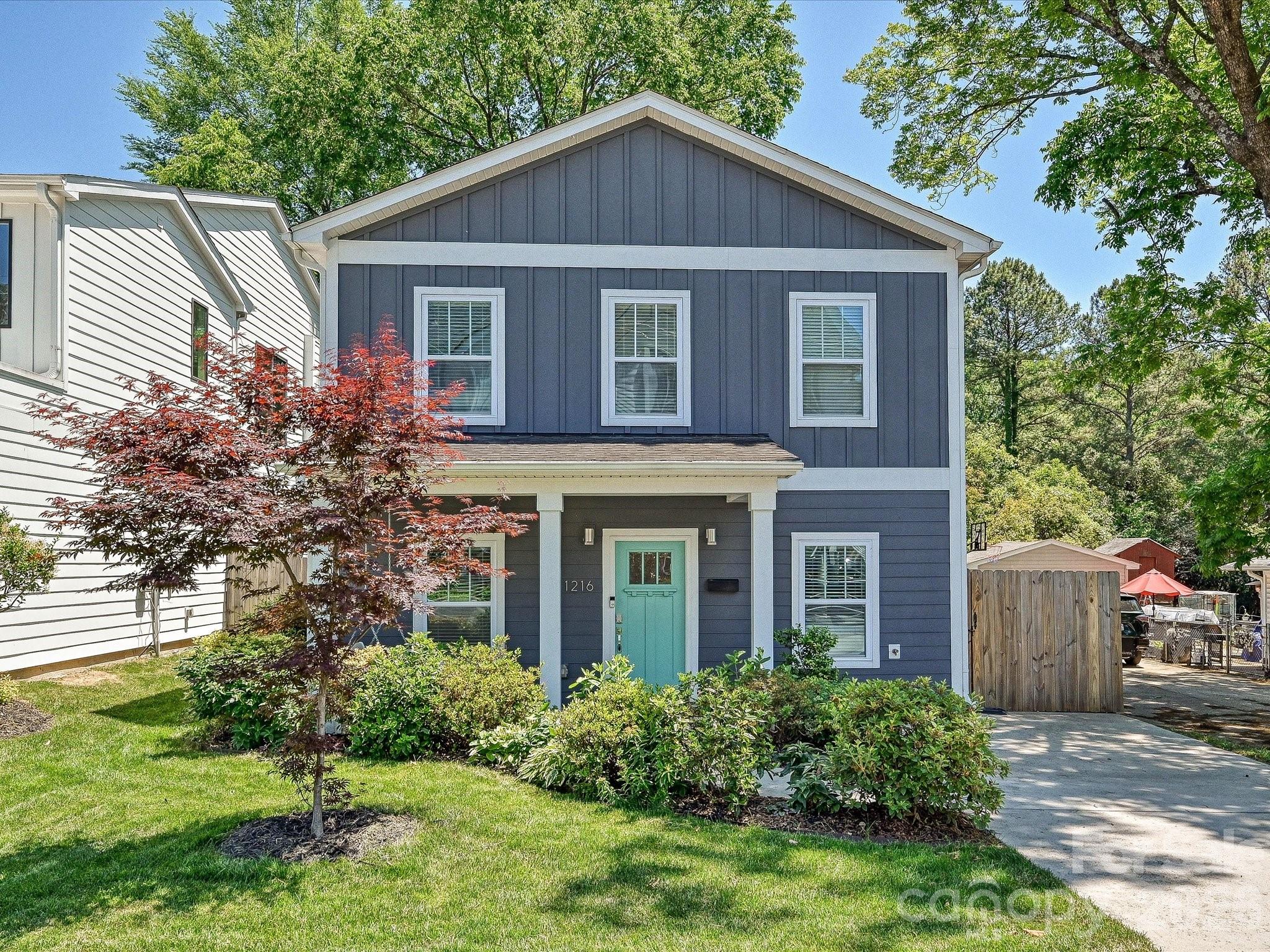 Two-story blue-gray house with a turquoise front door, white trim, and landscaped front yard.
