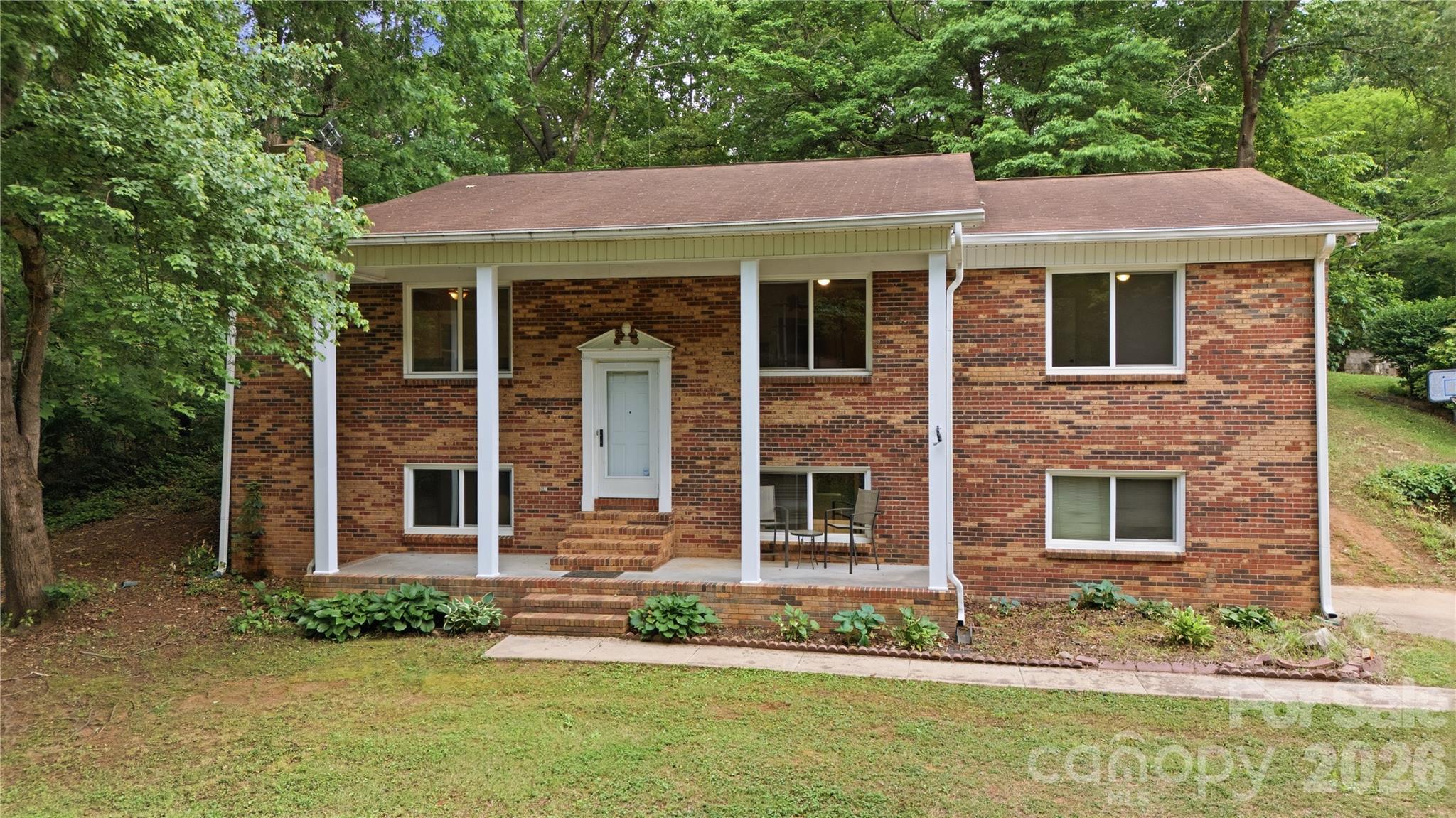Red brick house with a covered entrance, brick steps, and mature trees around the yard.