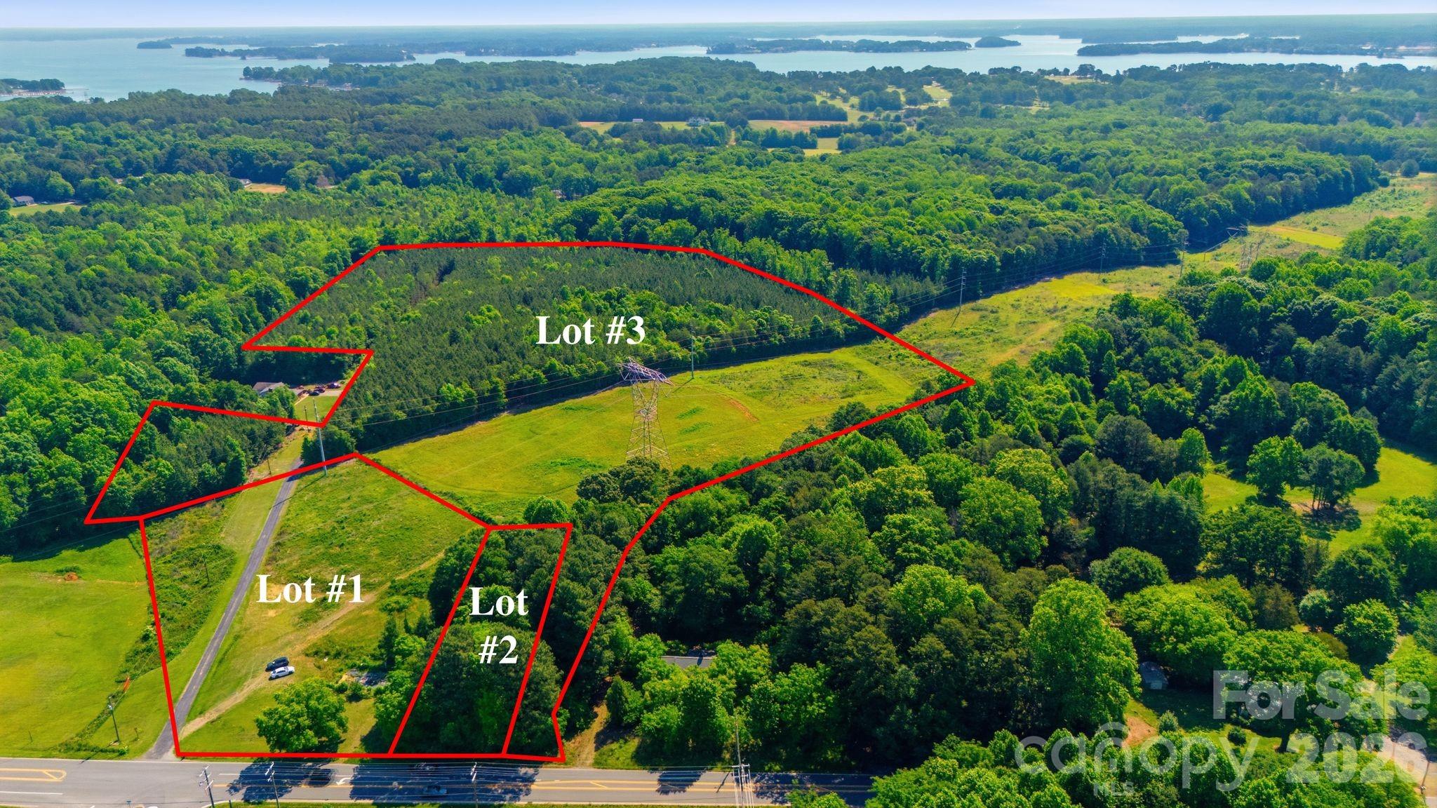 Aerial view of three outlined land lots, with wooded acreage, open fields, power lines, and a lake beyond.