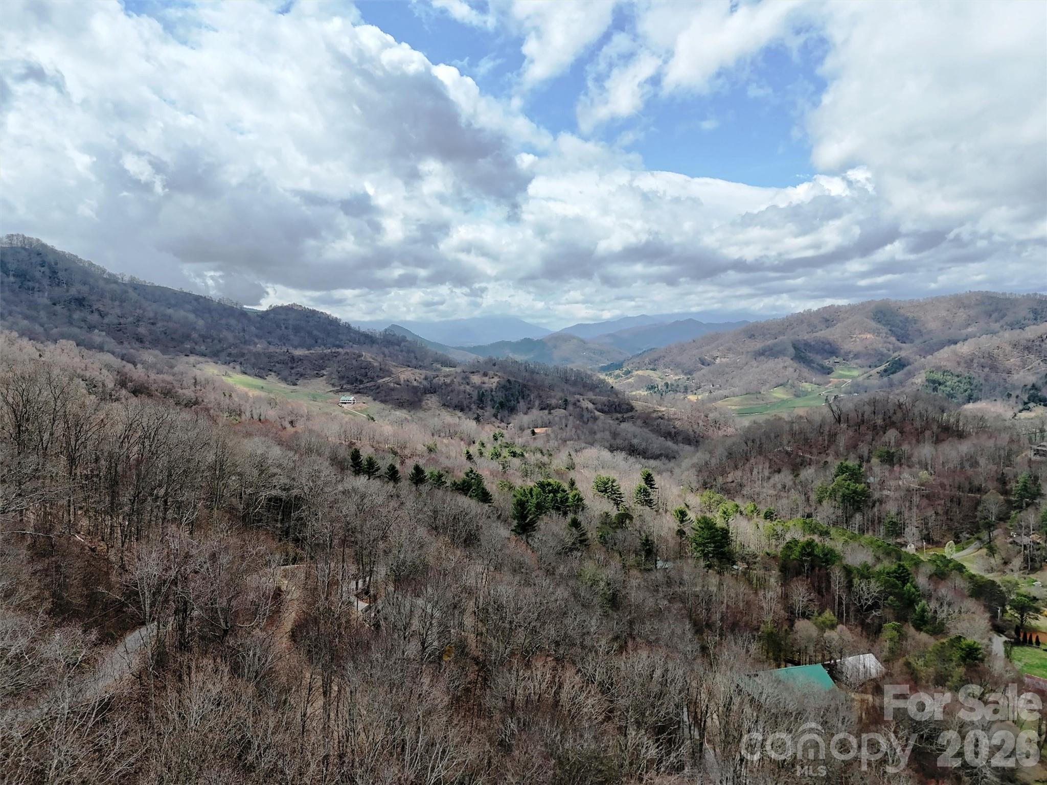 Aerial view of a wooded mountain valley with distant ridges and scattered homes.