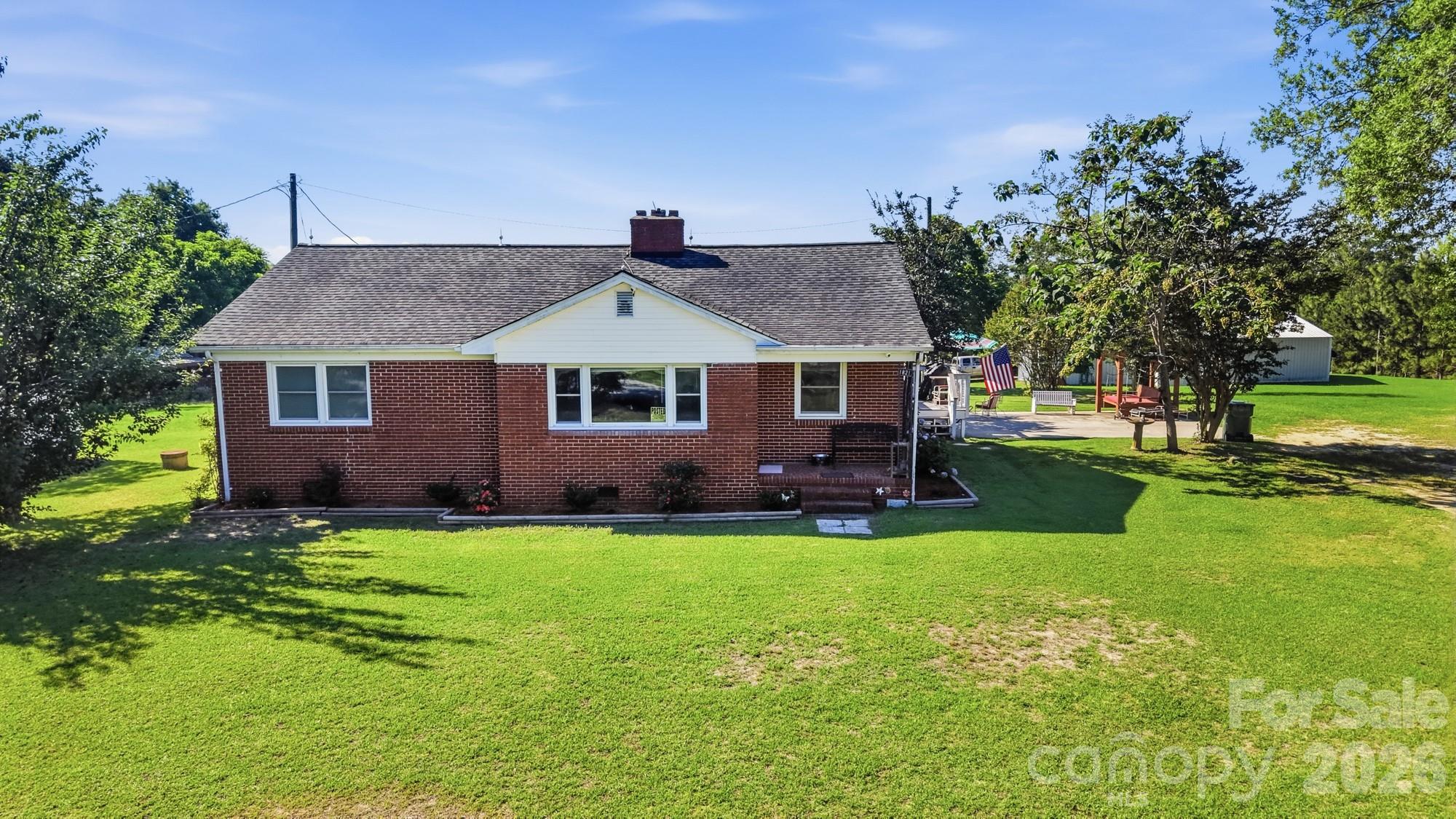 Red-brick ranch house with a white front gable, expansive lawn, and a flag beside the patio.