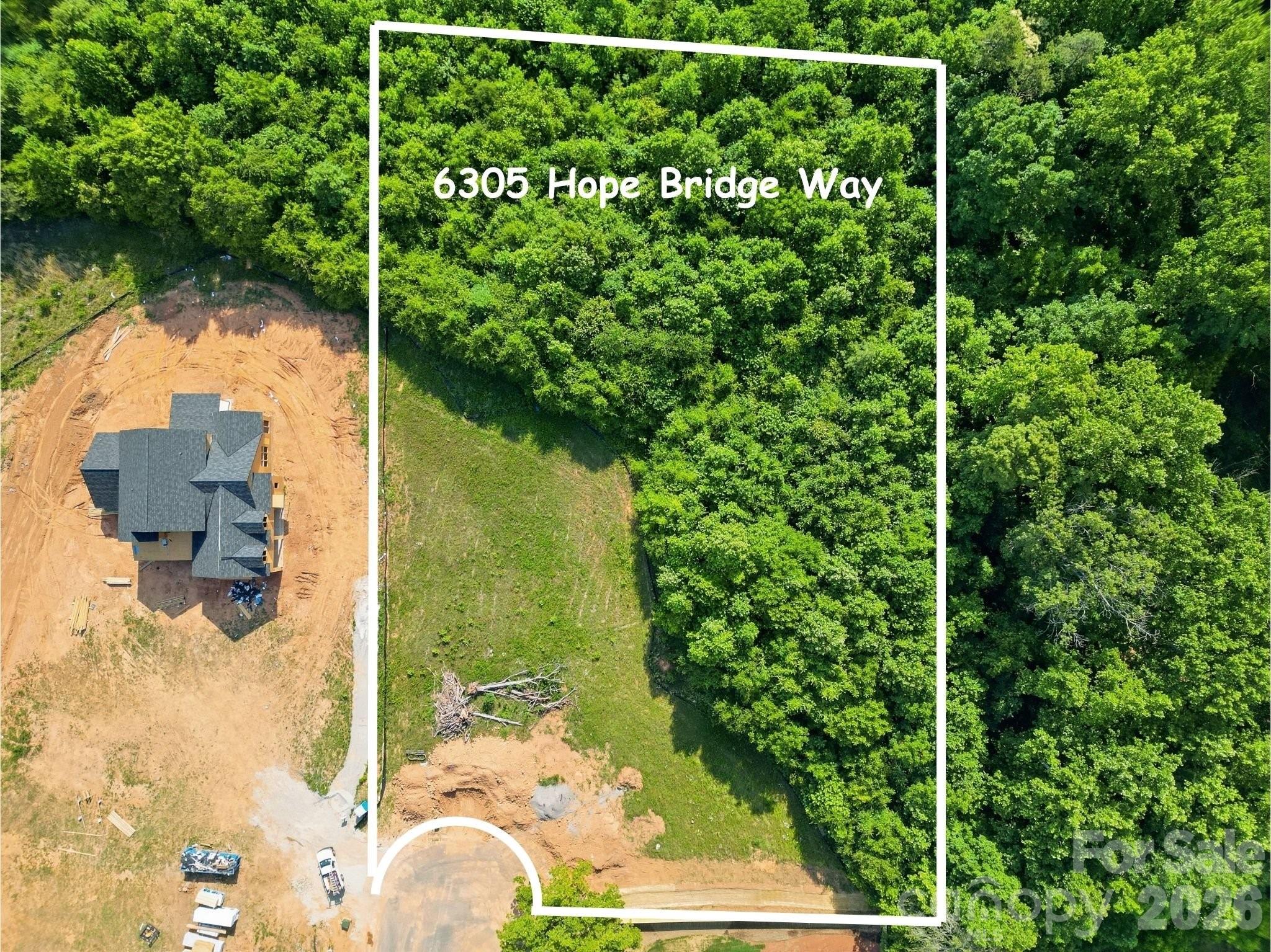 Aerial view of 6305 Hope Bridge Way, with a house under construction beside a wooded lot.