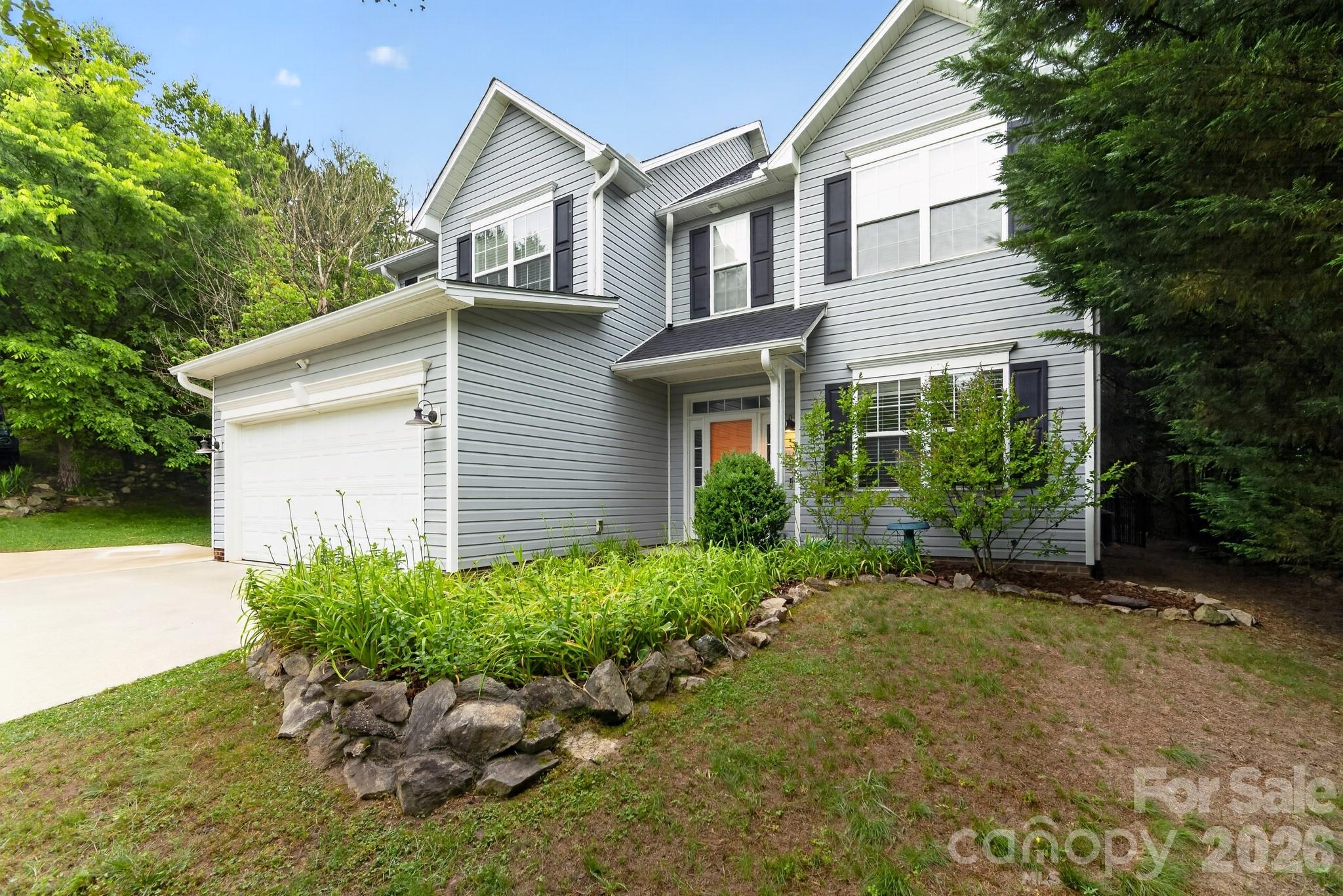 Two-story gray house with an attached garage, orange front door, and rock-edged garden beds.