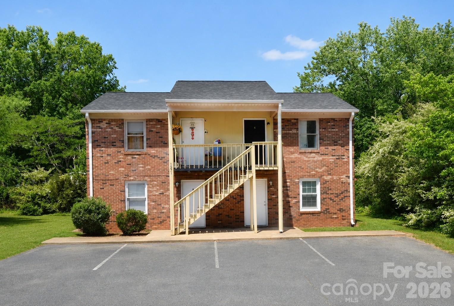 Two-story brick residential building with a central outdoor staircase, balconies, and parking in front.
