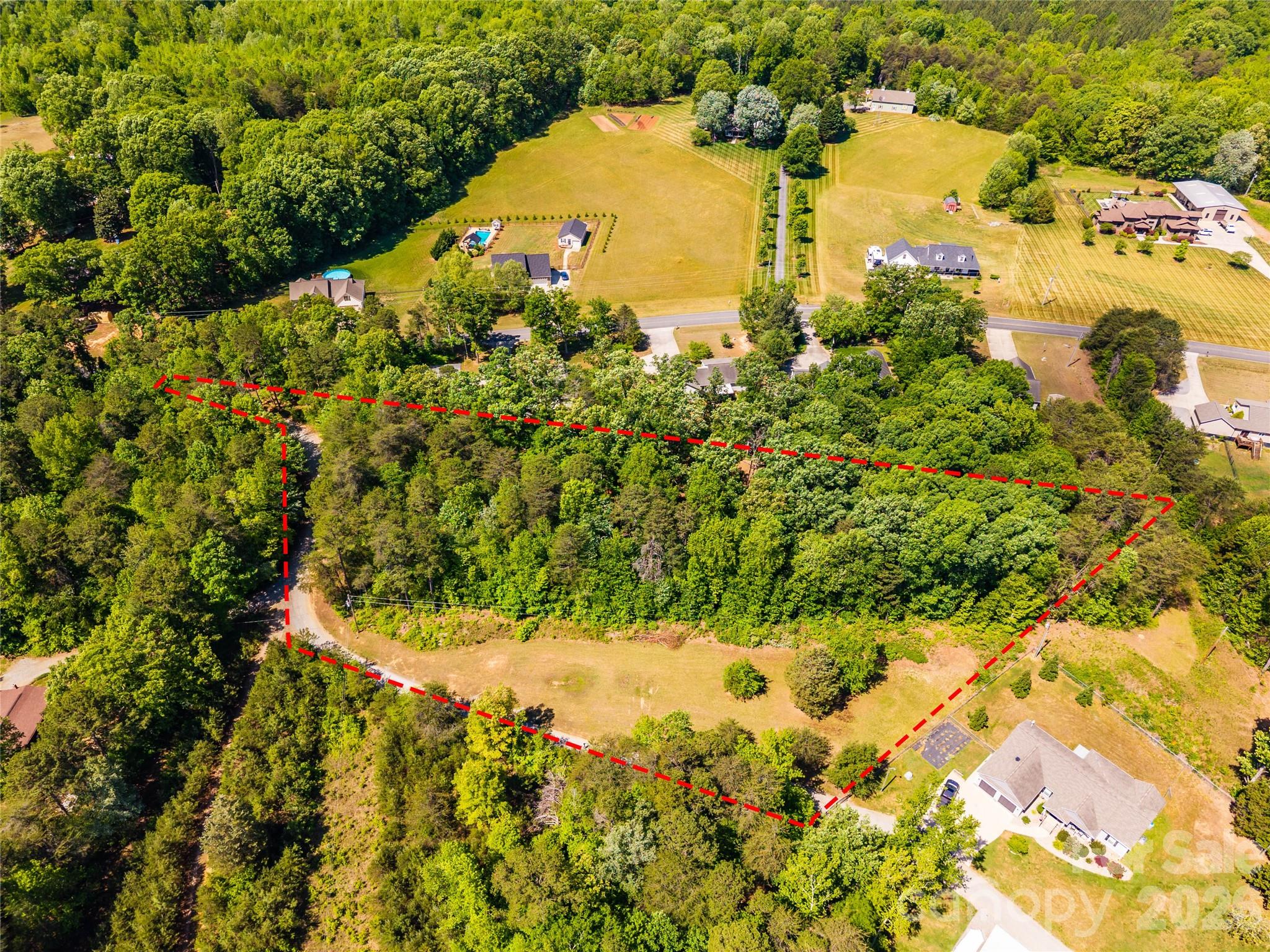 Aerial view of wooded vacant land outlined in red, with a clearing and nearby homes.