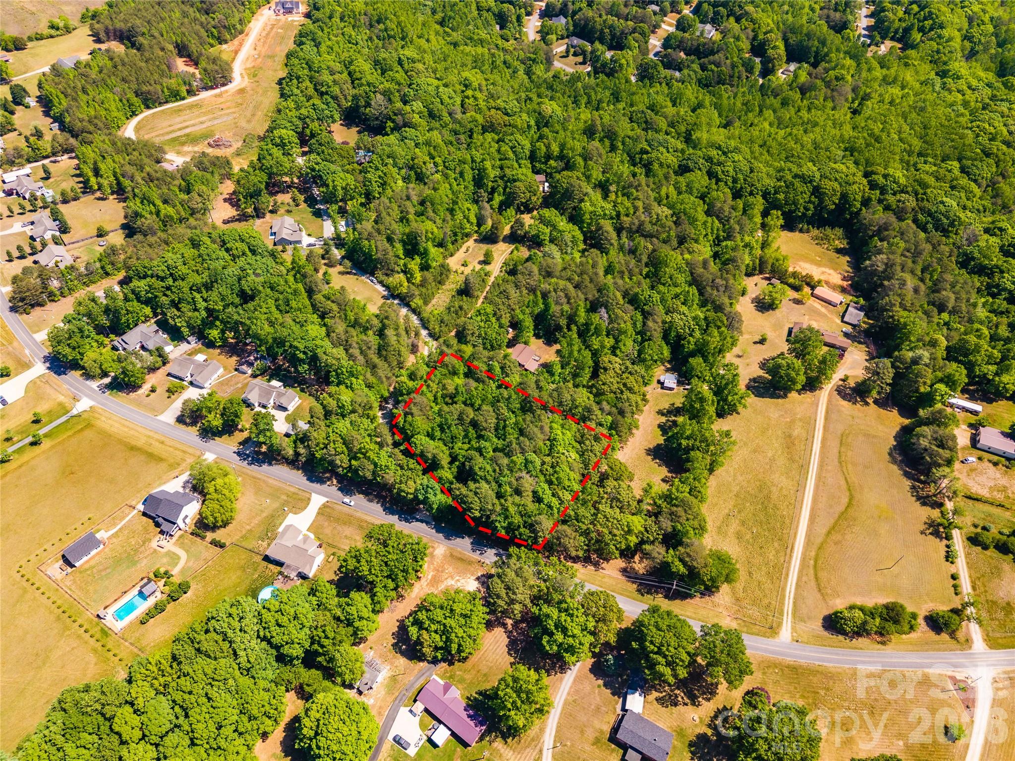 Aerial view of a wooded parcel outlined in red beside a rural road.