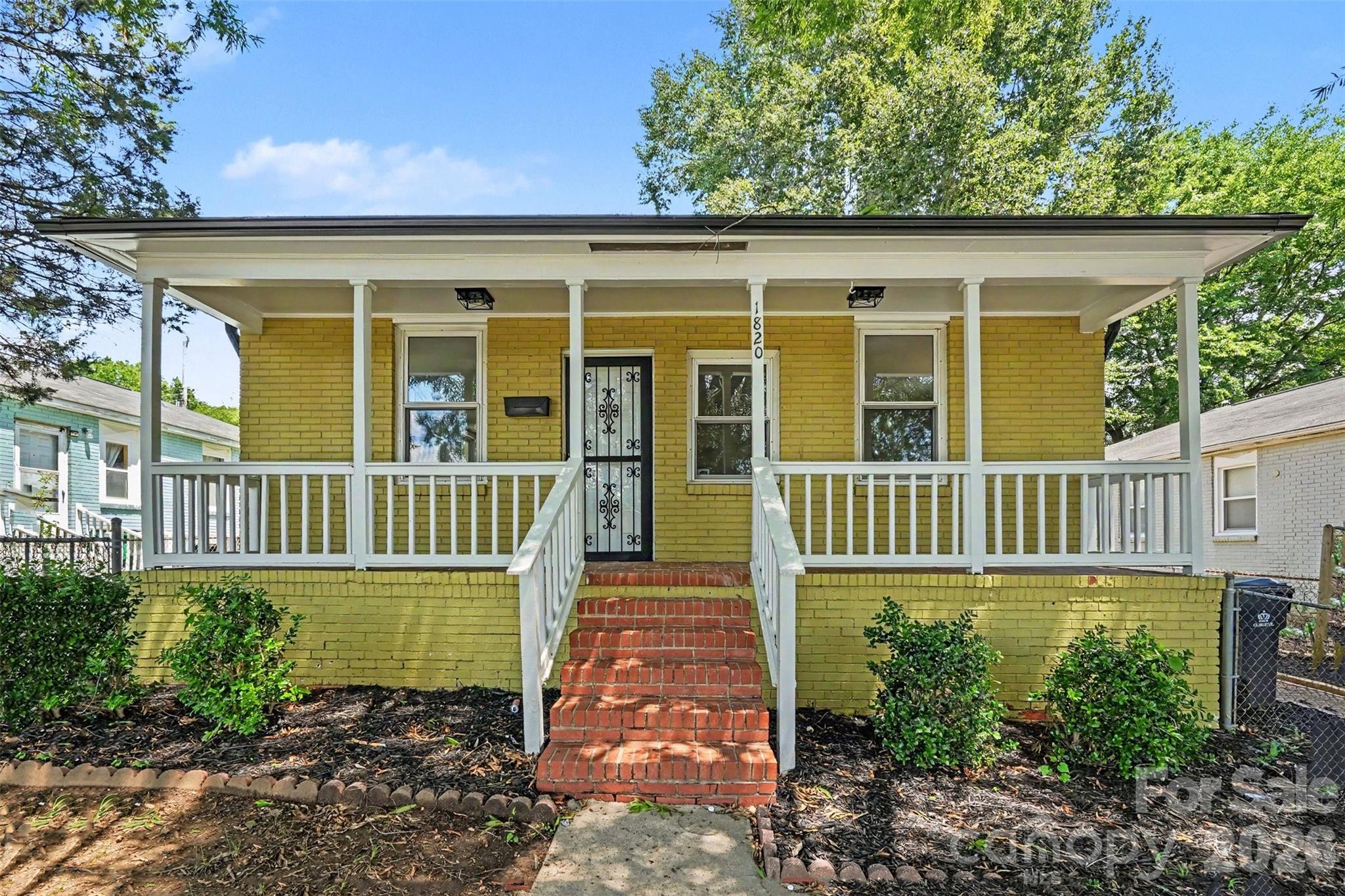 Yellow brick house with a wide white porch and red brick front steps.