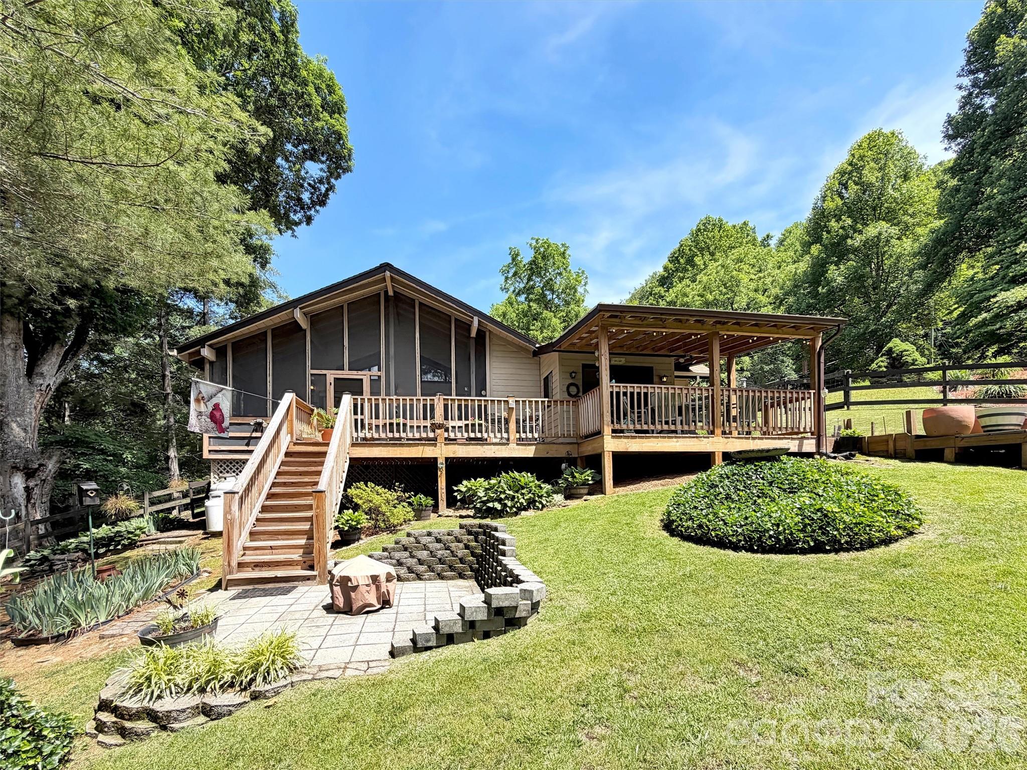 Single-story home with a raised wooden deck, covered porch, landscaped patio, and sloping lawn.