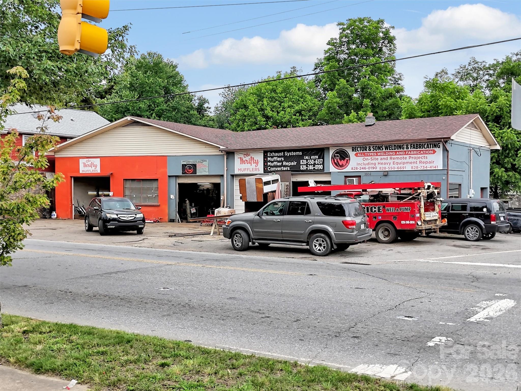 Commercial repair shop with orange and blue-gray storefronts, welding signs, and vehicles parked outside.