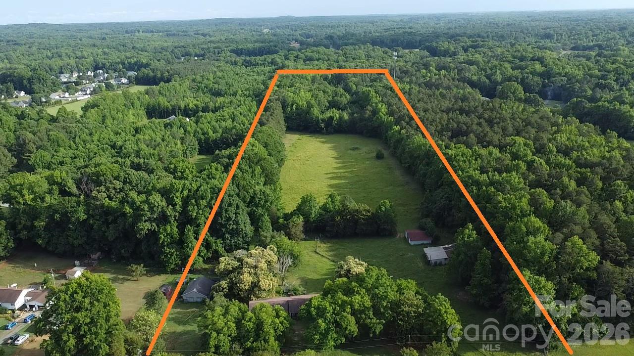 Aerial view of a wooded property outlined in orange, with a central clearing and several outbuildings.