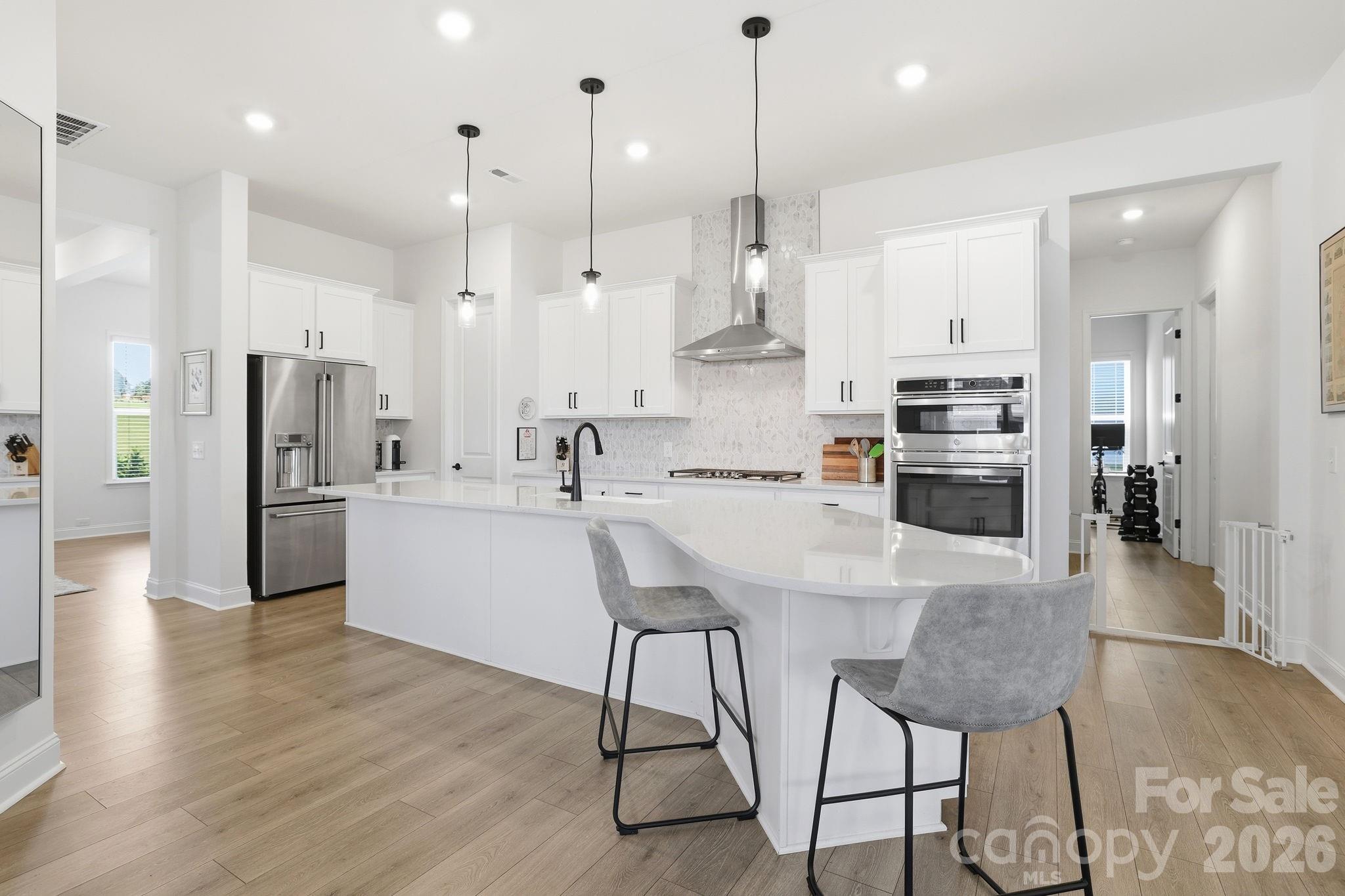 Modern white kitchen with a curved island, stainless steel appliances, and pendant lights.