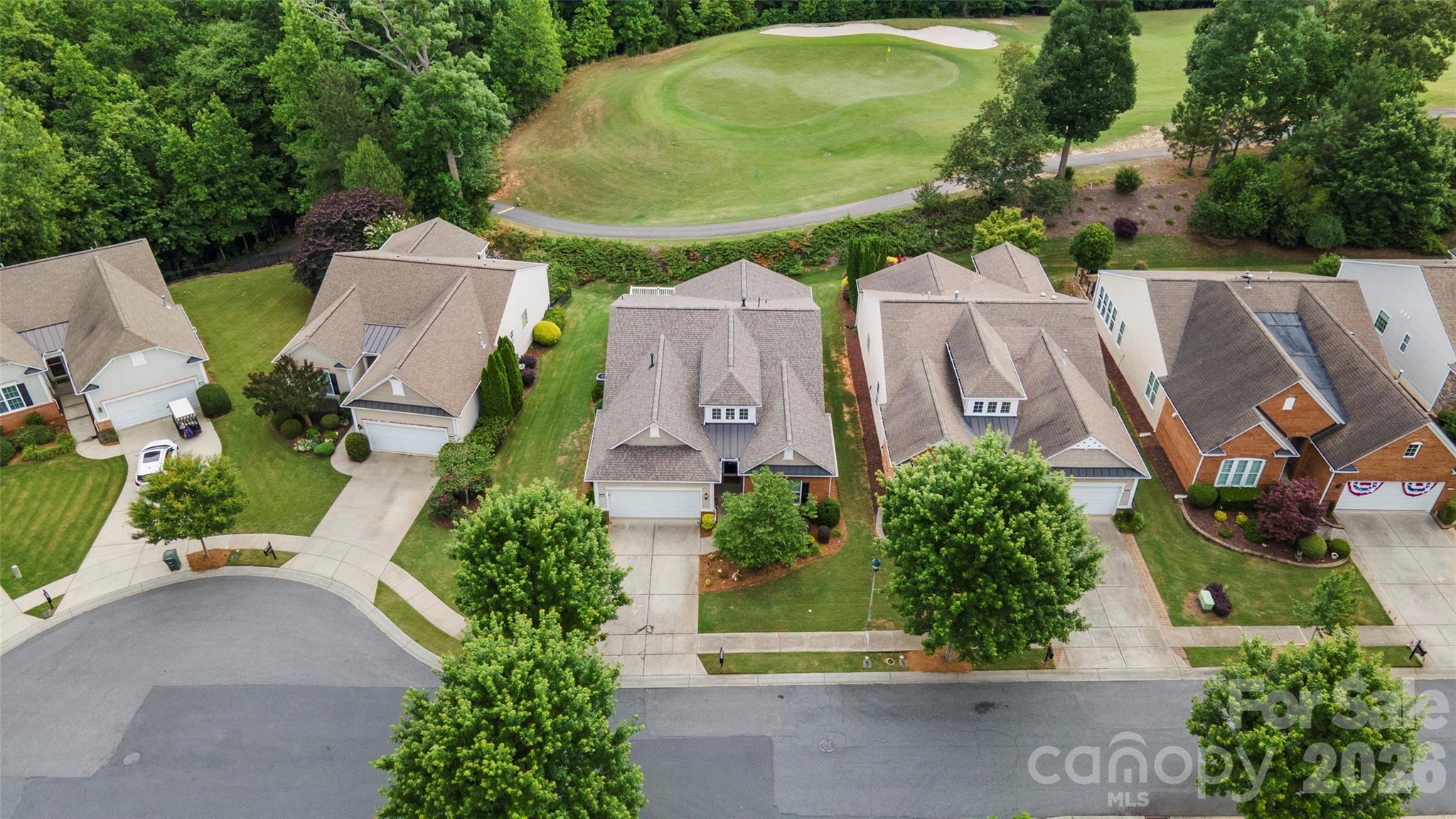 Aerial view of homes beside a golf course green, with mature trees and landscaped yards.