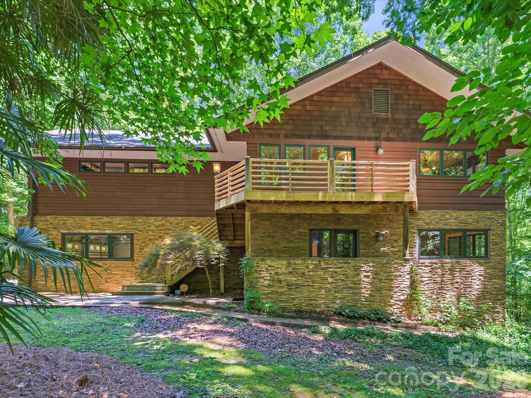 Wood-and-stone home with a raised deck nestled among mature trees.