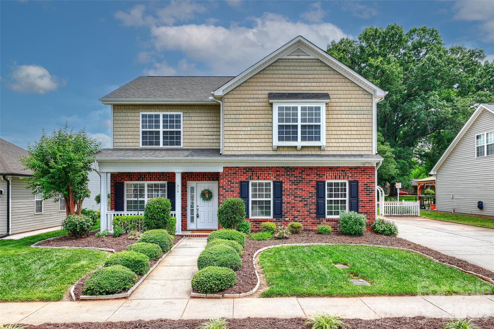 Two-story brick and shingle house with a covered porch and landscaped front yard.