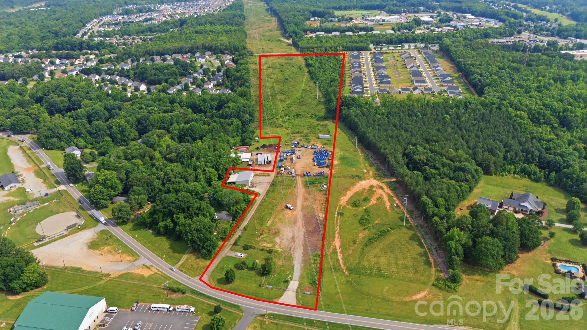 Aerial view of a red-outlined parcel with wooded land, utility lines, and a cleared work area.