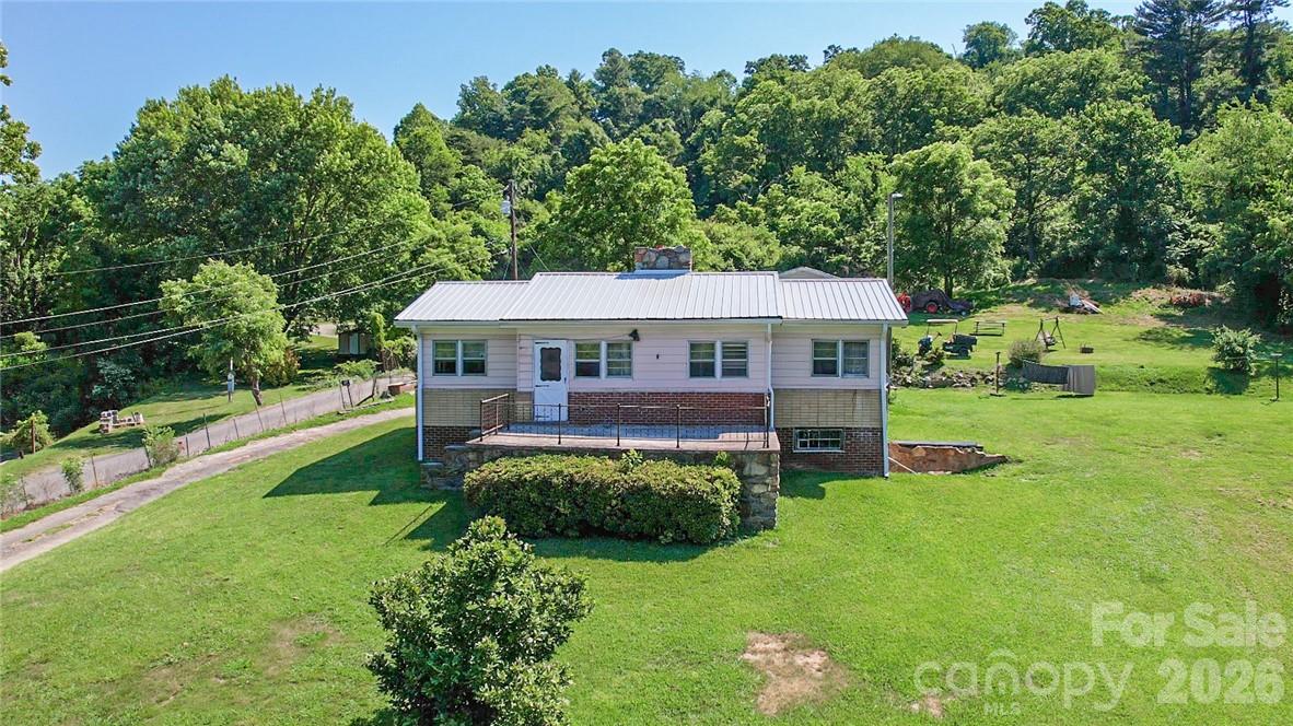 Single-story home with a metal roof and raised front porch on a large wooded lot.