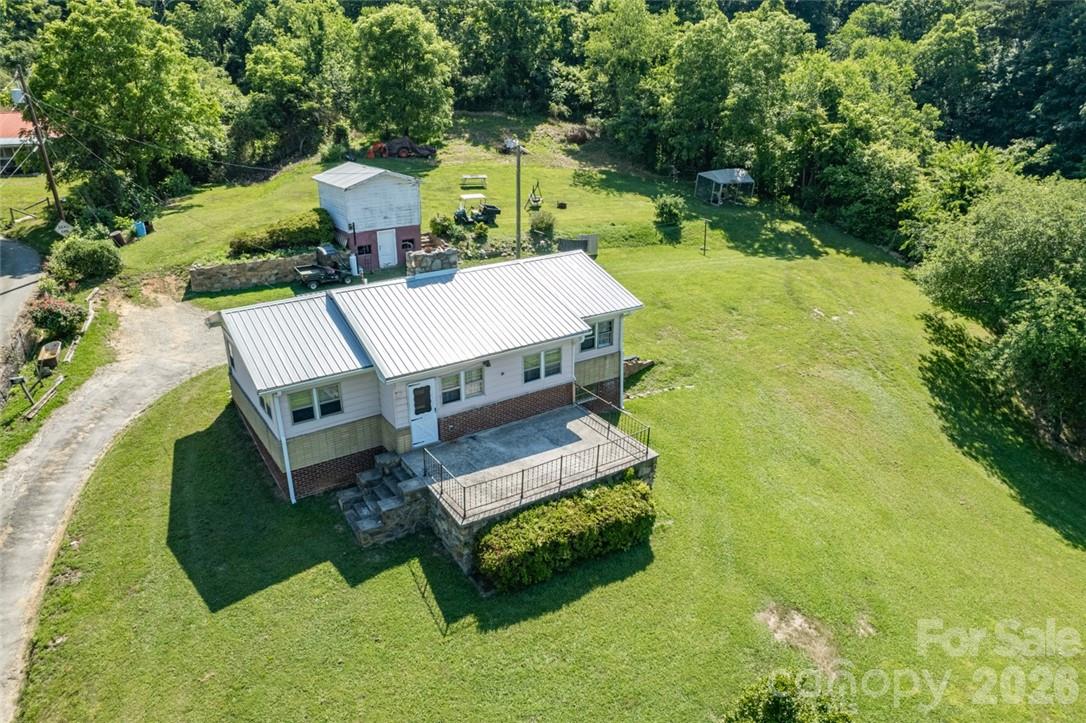 Aerial view of a single-story home with a metal roof, raised porch, and expansive lawn.