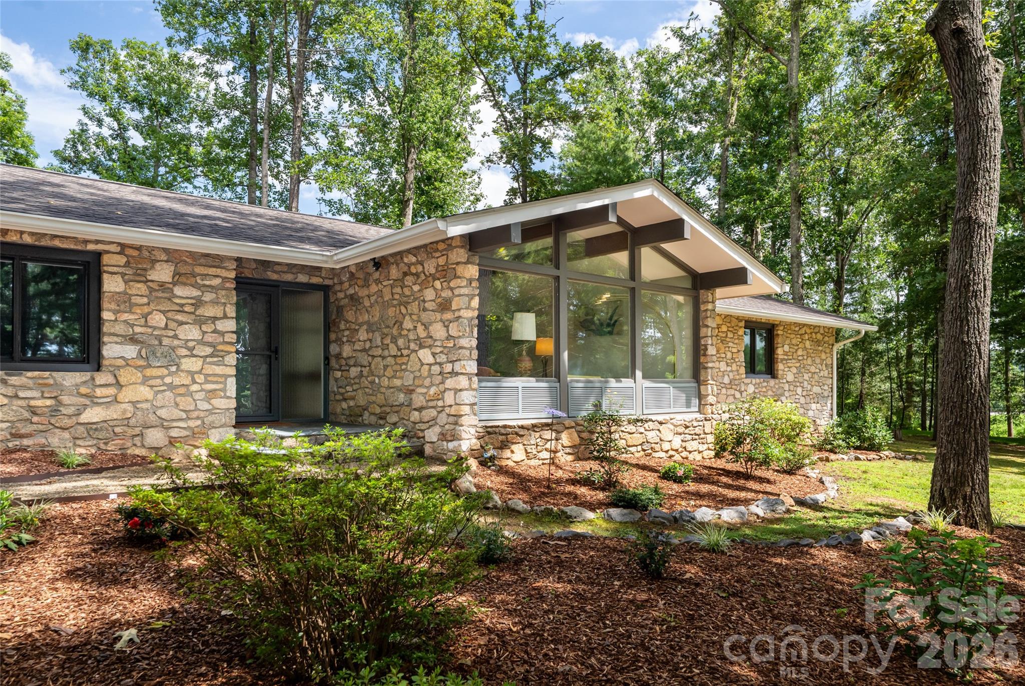 Stone house with a dramatic angled roof and tall windows, set among mature trees and landscaped grounds.