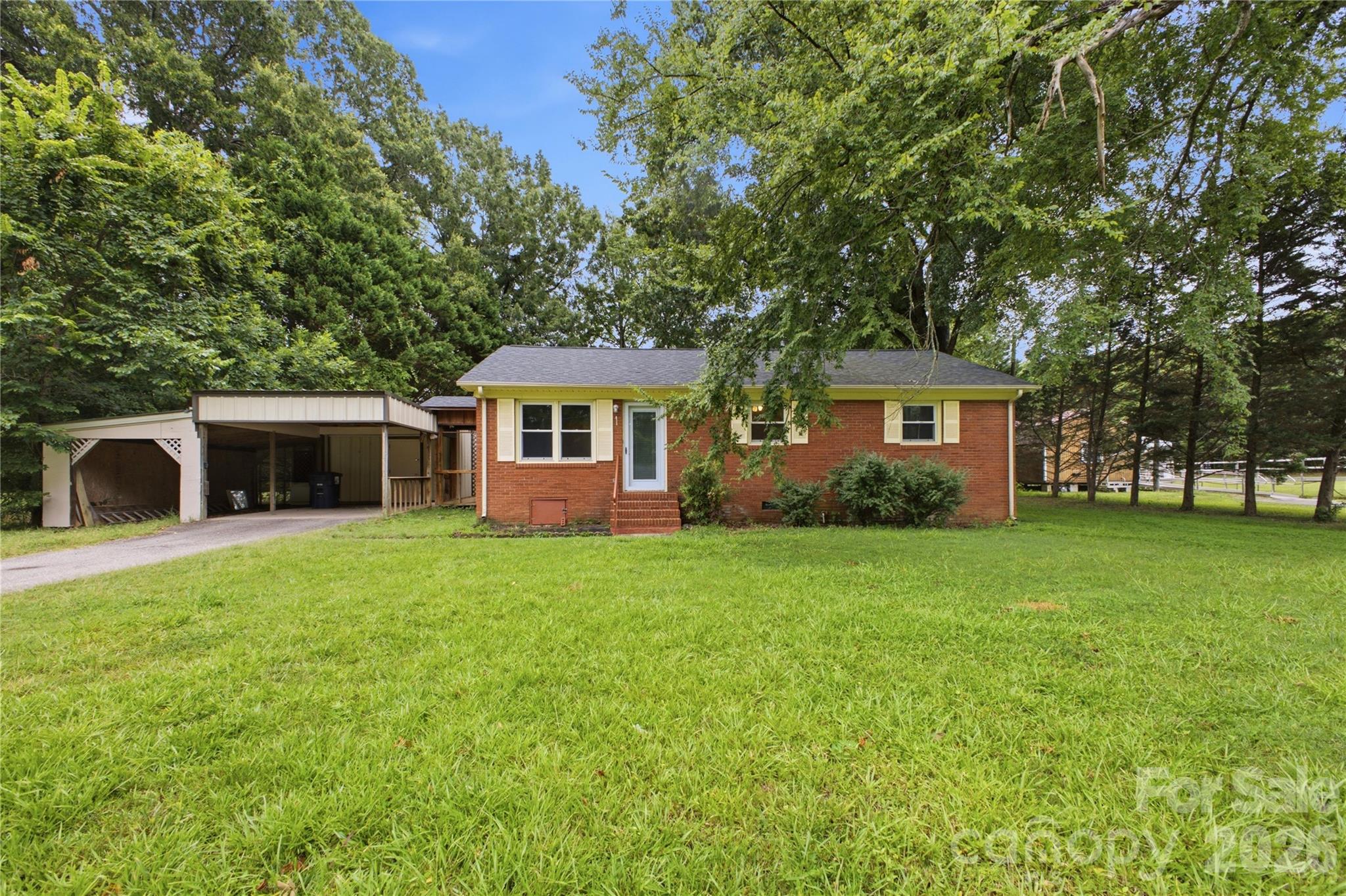 Red brick ranch house with a covered carport, broad lawn, and mature trees.