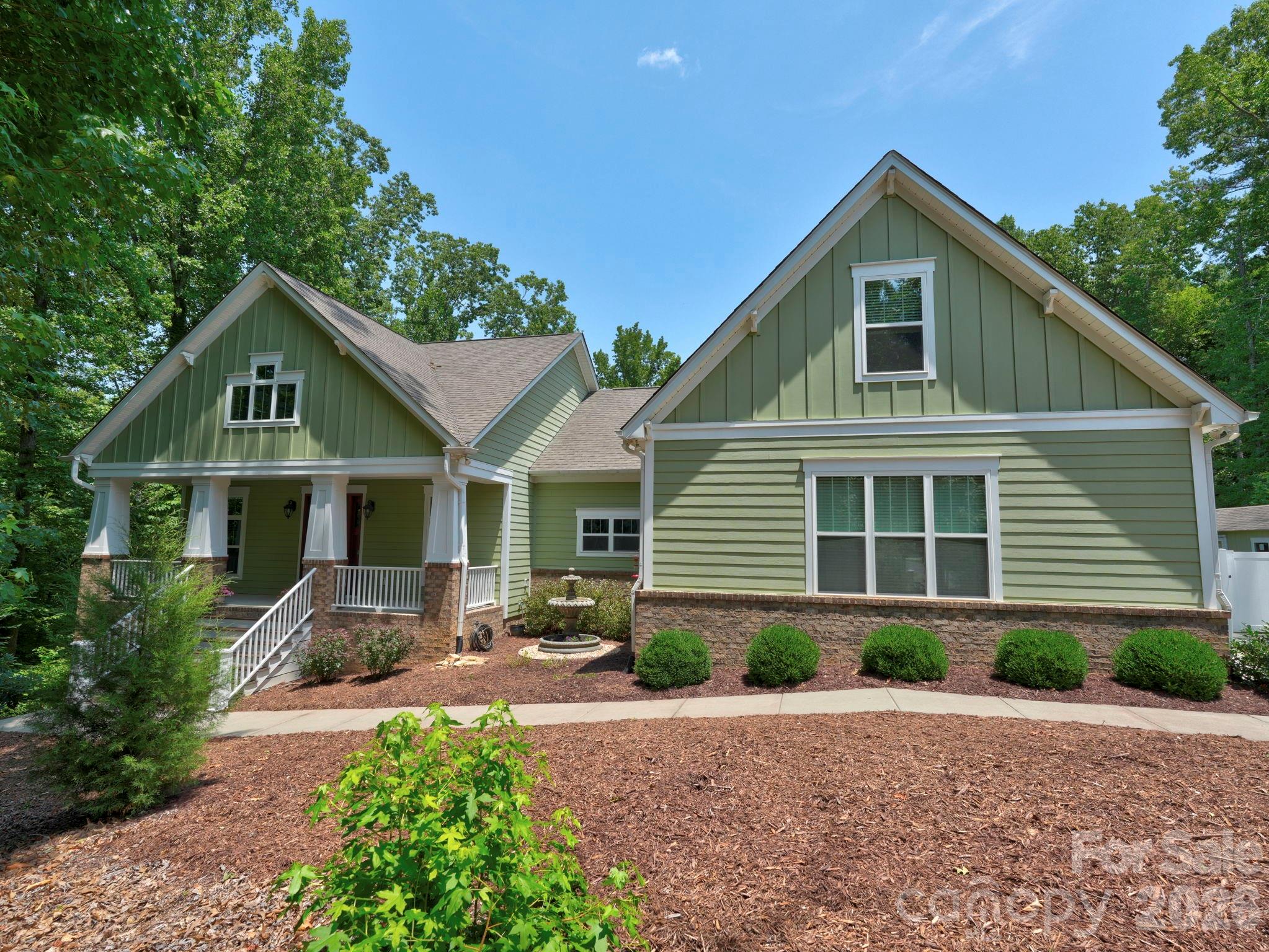 Green house with white-trimmed covered porch, stone foundation, and landscaped front yard.