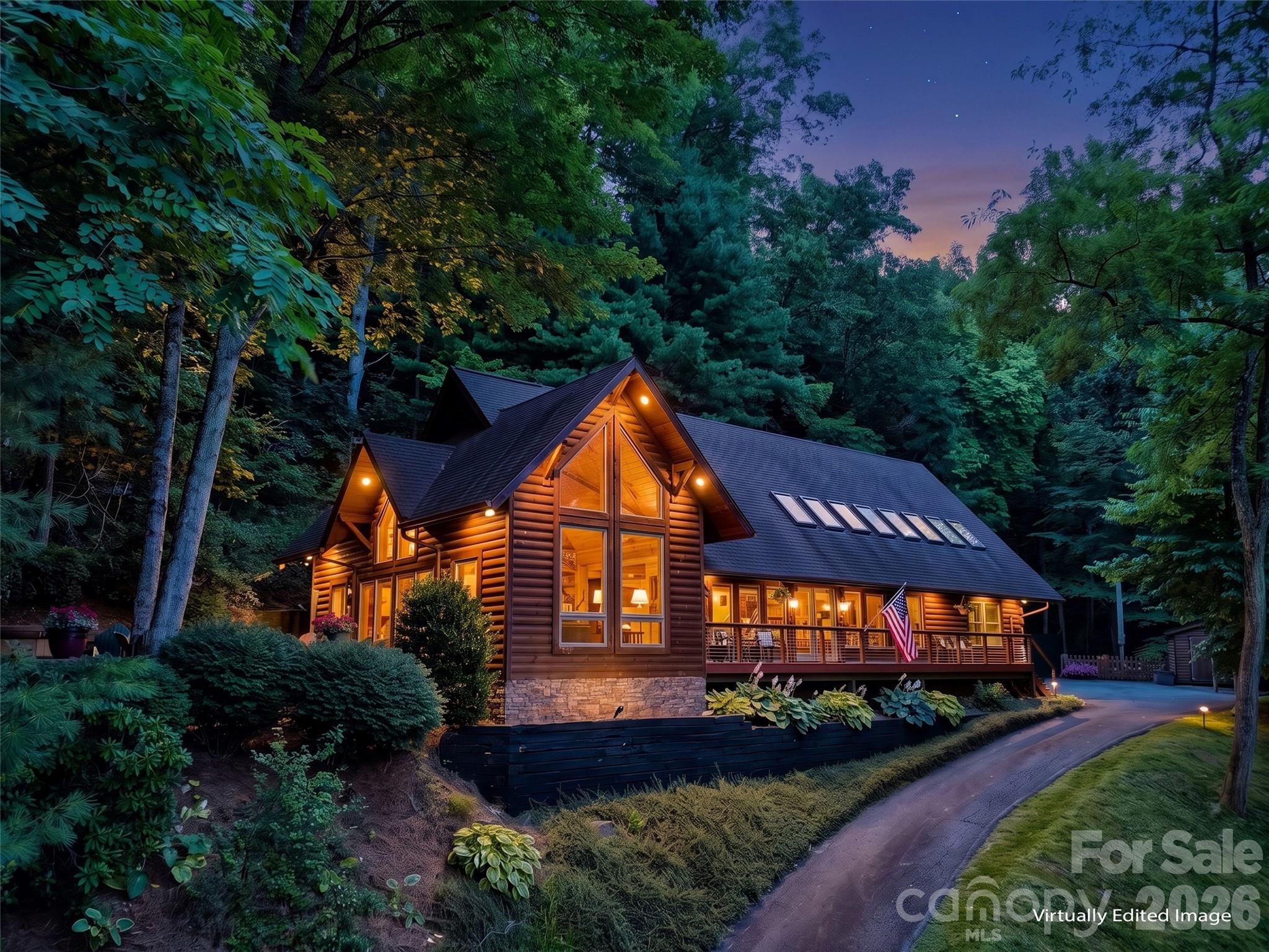 Wooded log cabin home at dusk with glowing windows, a long deck, and skylights.