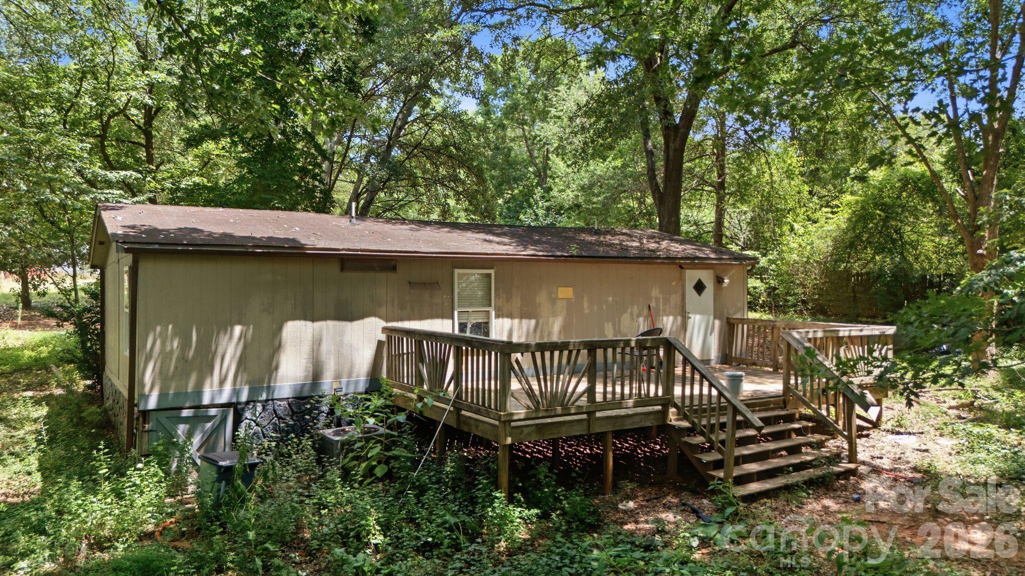 House rear exterior with a raised wooden deck and stairs in a wooded setting.