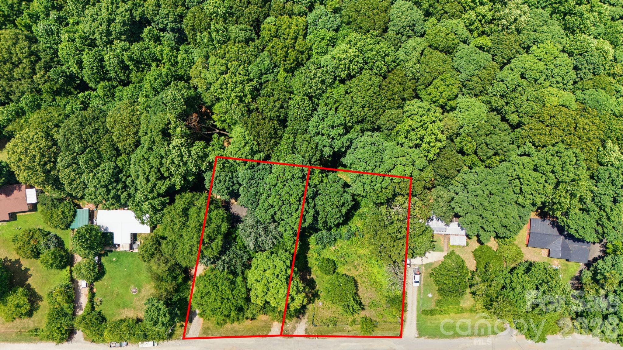 Aerial view of a wooded parcel outlined in red beside neighboring homes and a road.