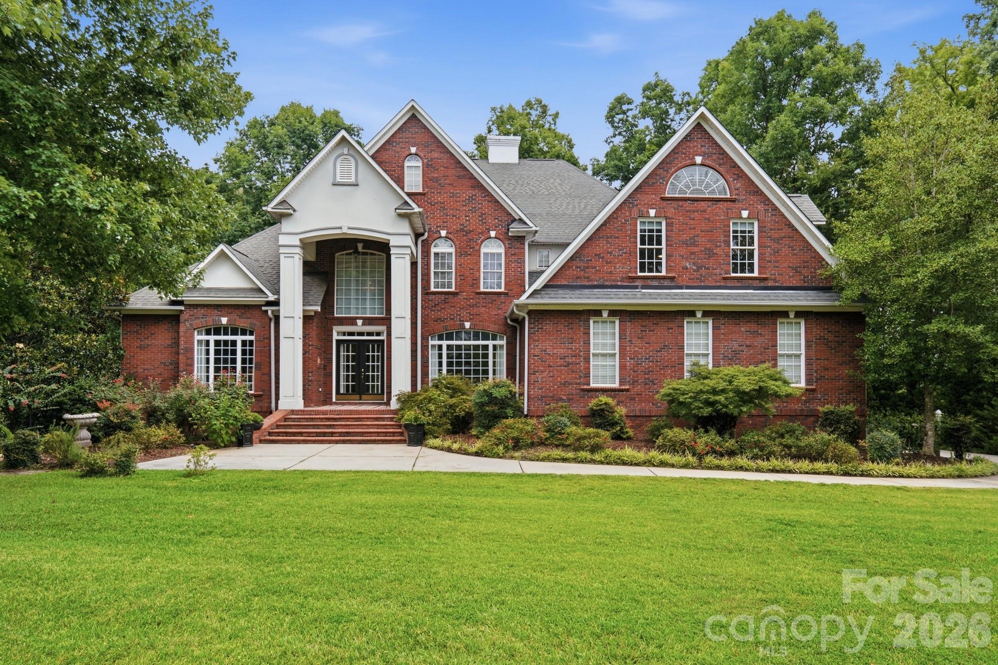 Red-brick house with multiple gables, arched windows, and a broad green lawn.