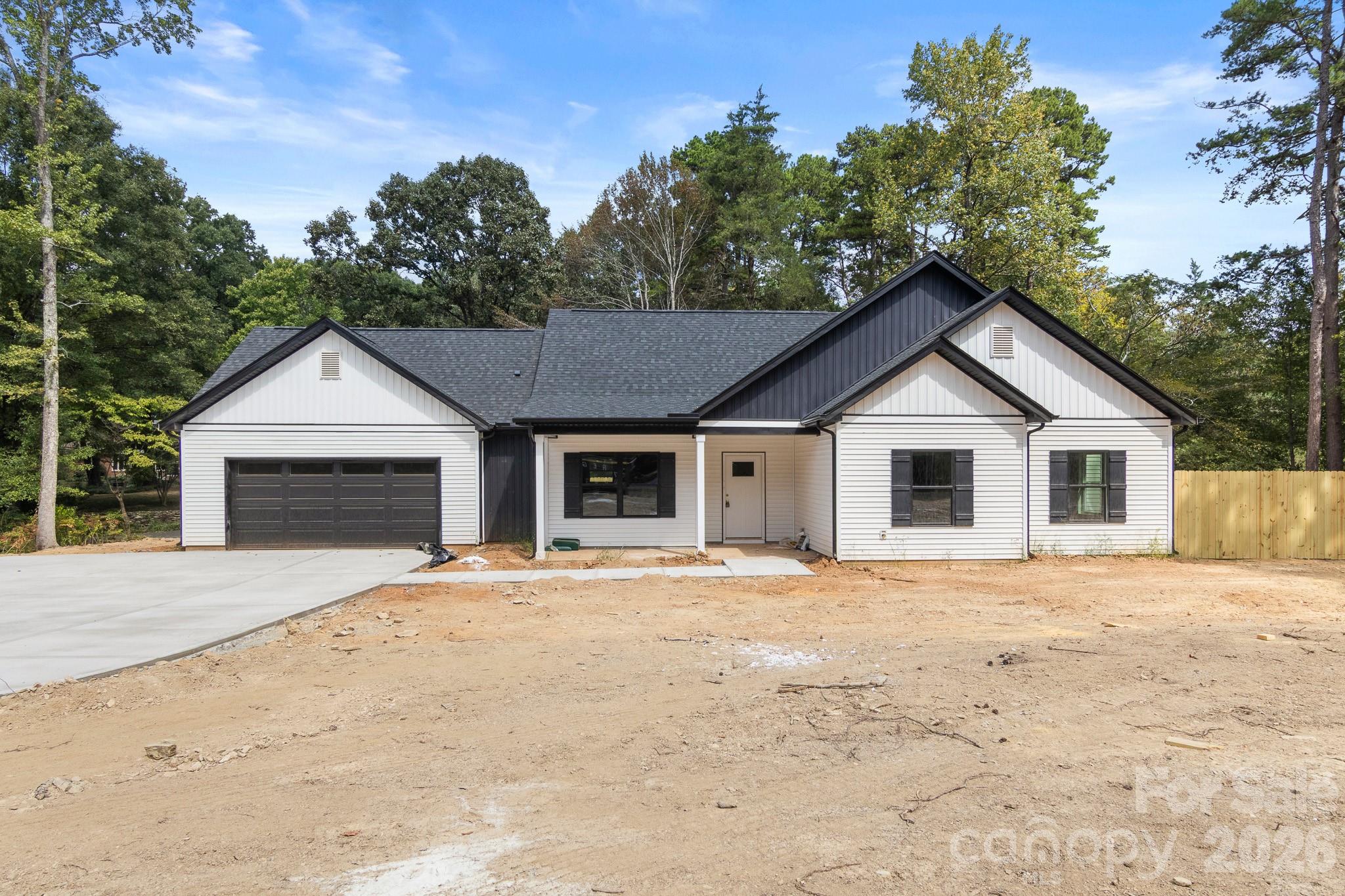 Single-story white house with dark gables, a two-car garage, and an unfinished dirt yard.
