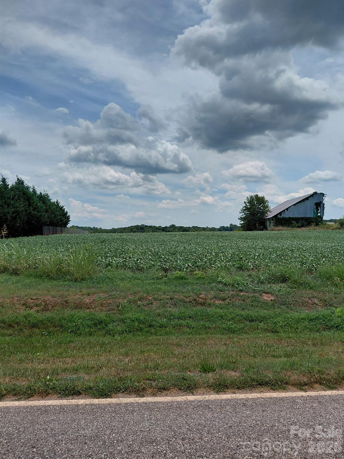 Rural field beside a road, with a weathered barn and dramatic clouds.