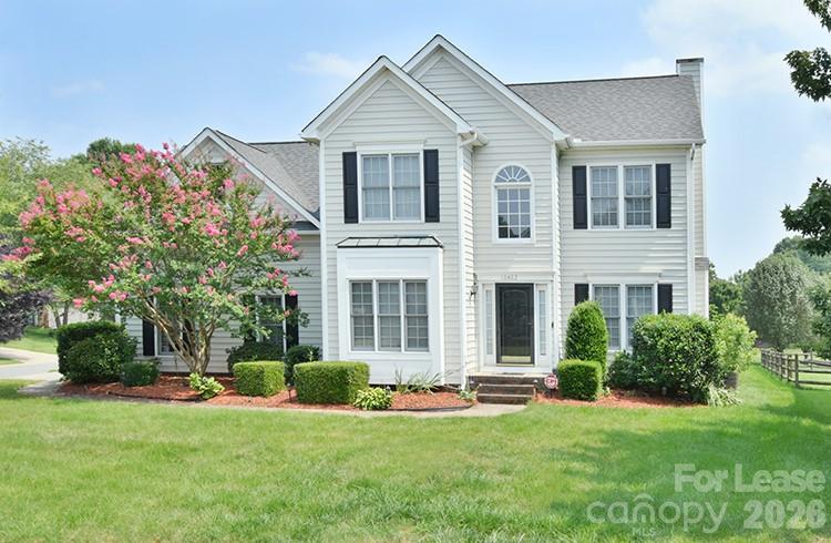 Two-story white house with black shutters, a pink-flowering tree, and a green front lawn.