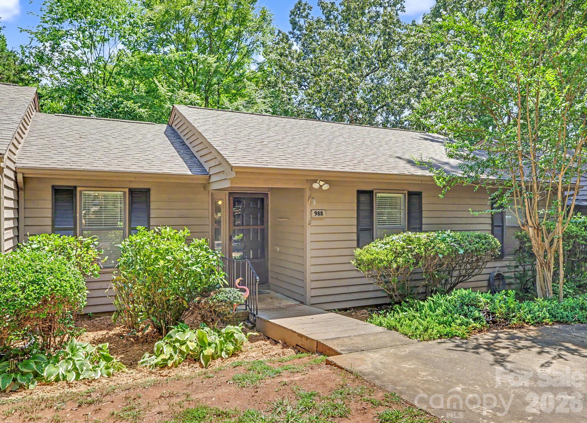 Single-story tan home with dark shutters, a front walkway, and mature landscaping.
