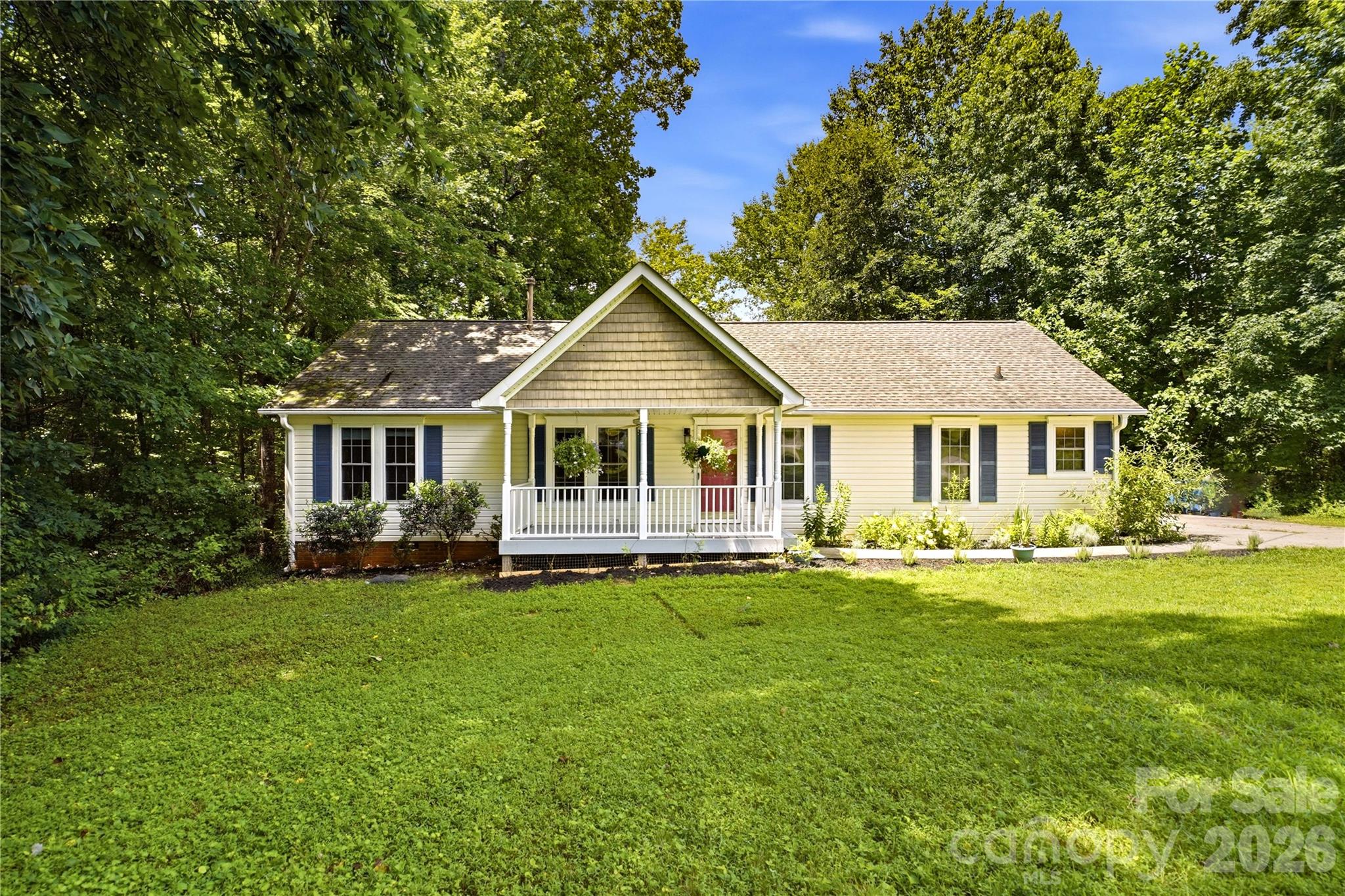 Cream-colored home with blue shutters, a covered porch, red front door, and broad green lawn.