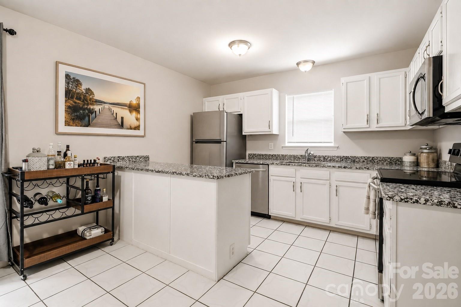 Kitchen with white cabinetry, stainless steel appliances, patterned counters, and a central peninsula.