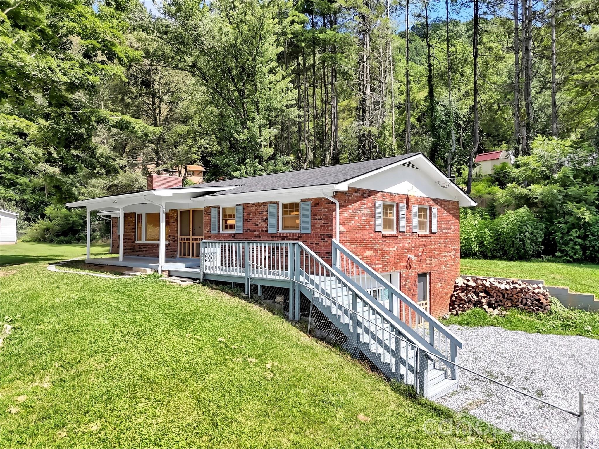 Red brick ranch home with a covered porch and long ramp on a wooded lot.