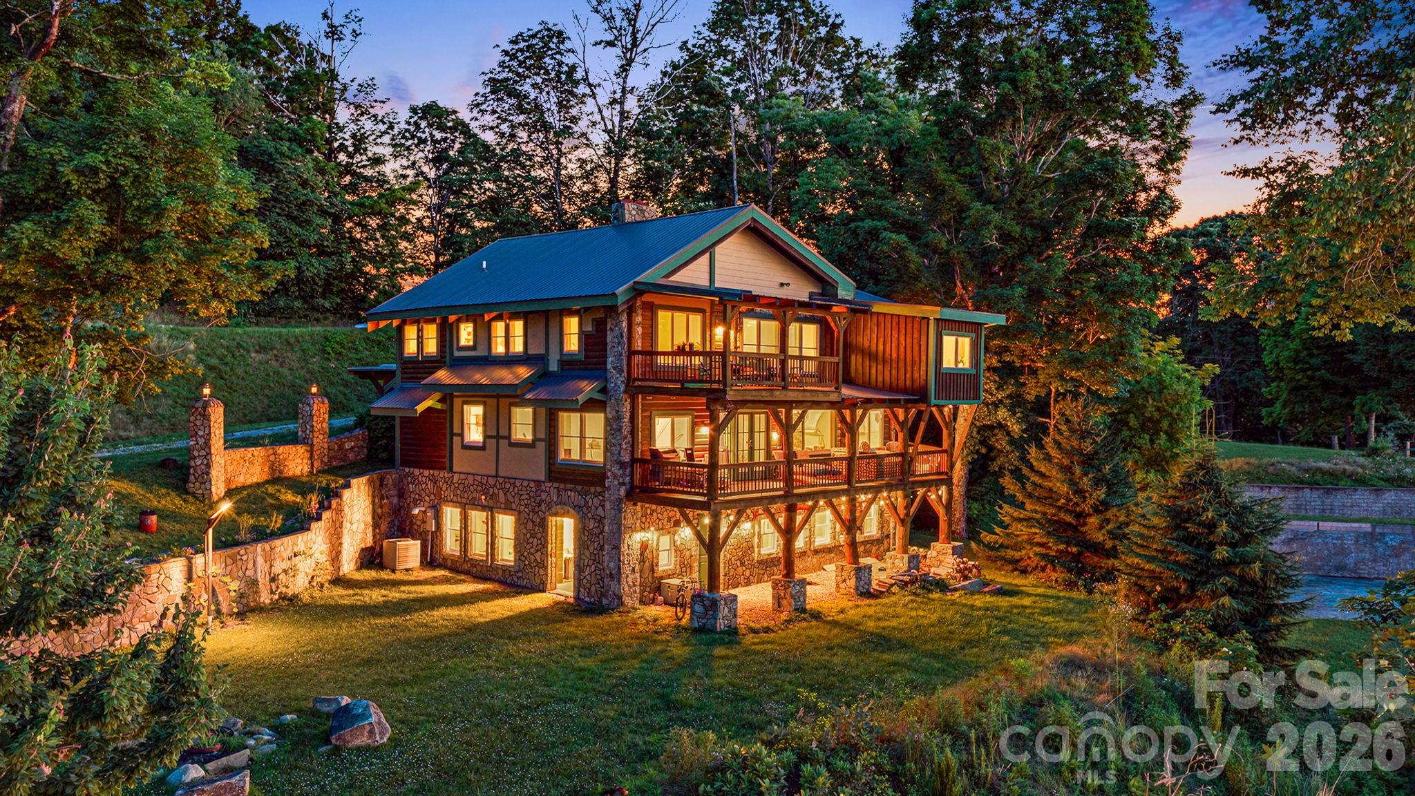 1185 Black Bear Drive, a rustic multi-level home with stone walls and timber balconies, glowing among trees at dusk.