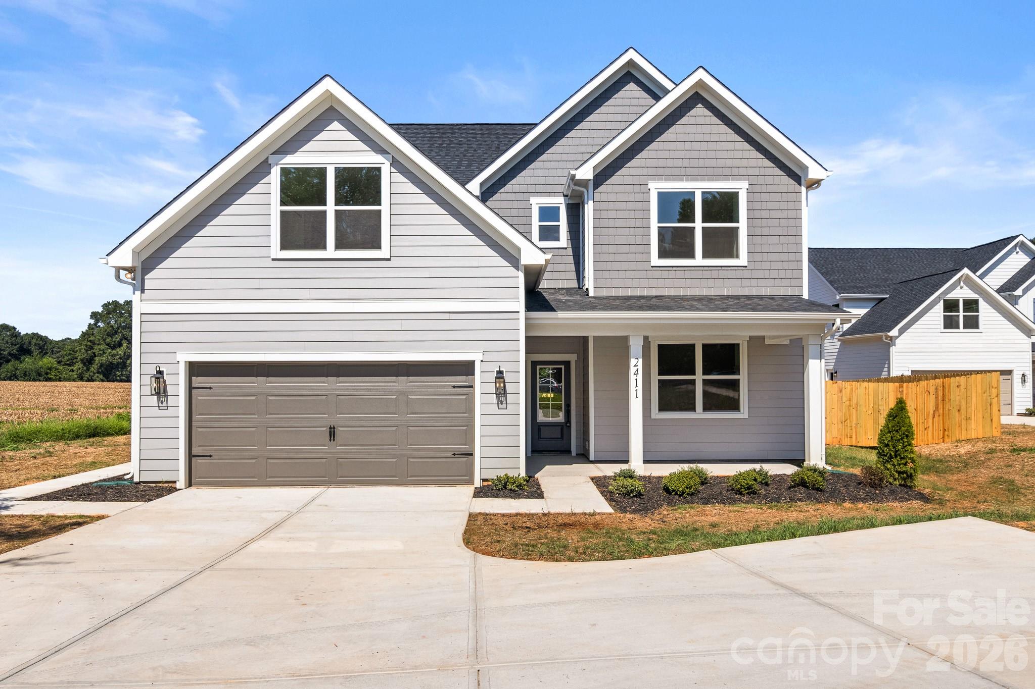 Gray two-story house with multiple gables, a double garage, and a wide concrete driveway.
