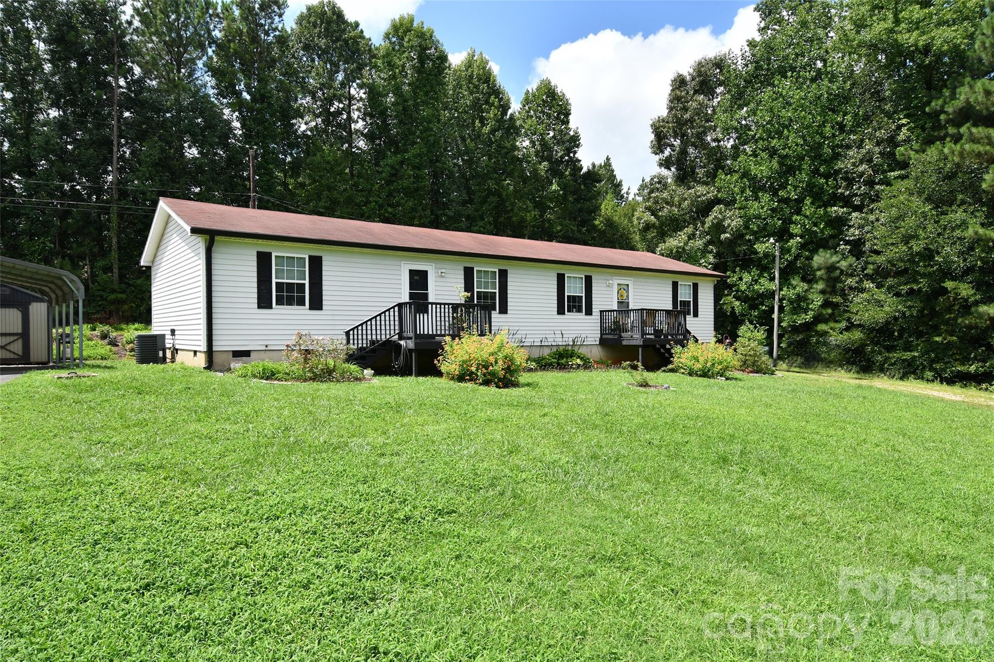 White single-story home with black shutters, two raised decks, and a broad lawn backed by trees.