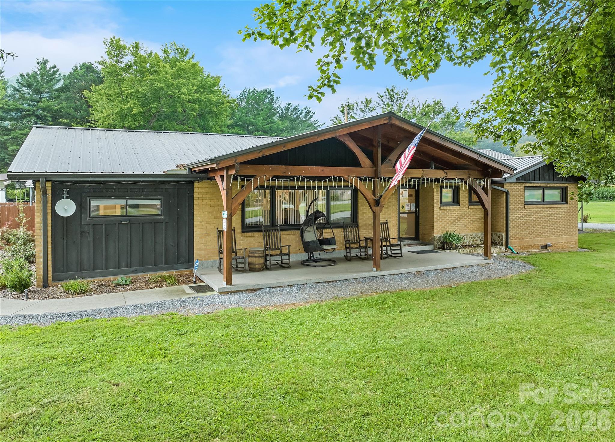 Brick home with a timber-framed porch, rocking chairs, American flag, and broad green lawn.