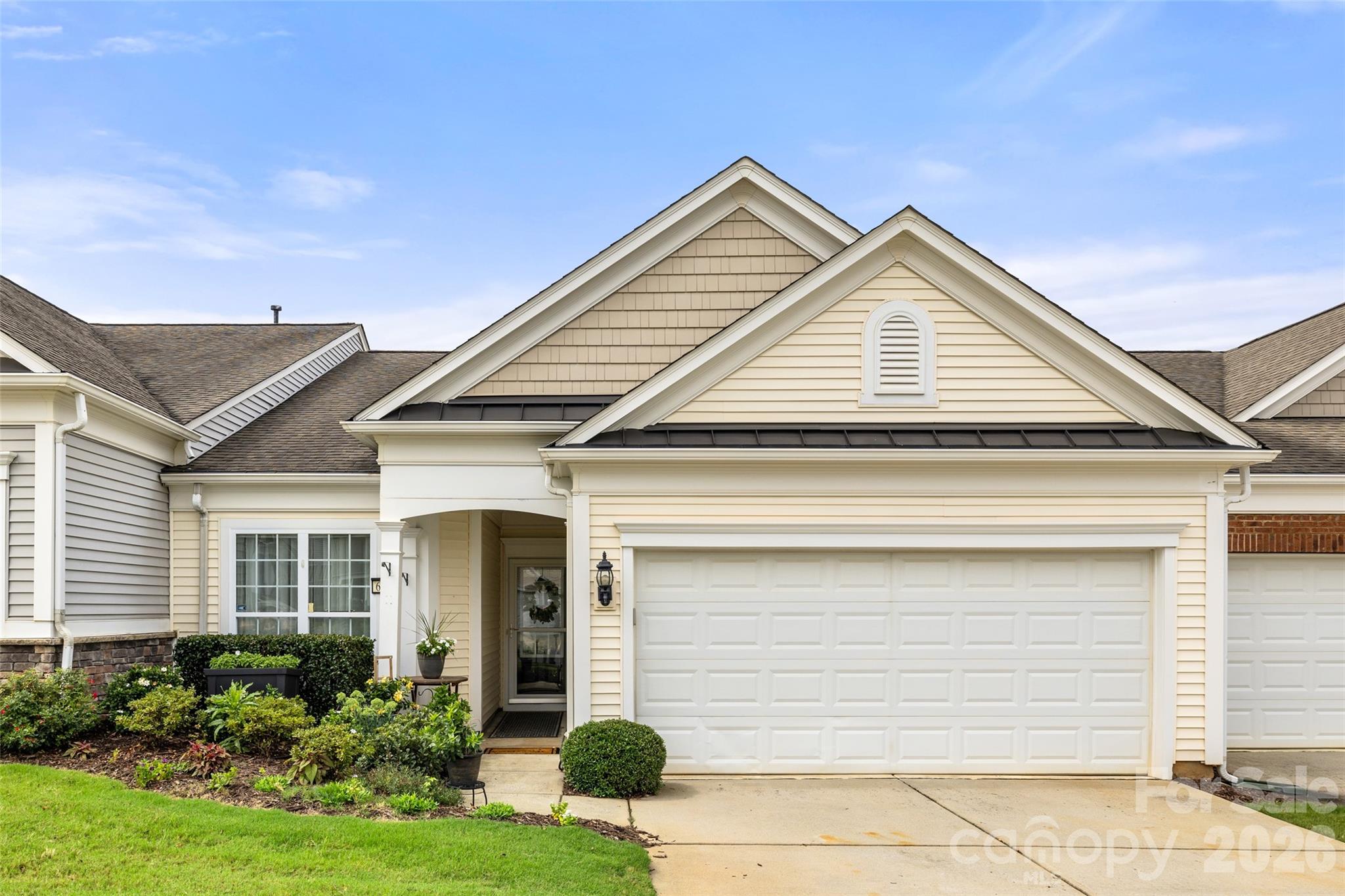 Beige home with a white two-car garage, intersecting gables, and landscaped front garden.