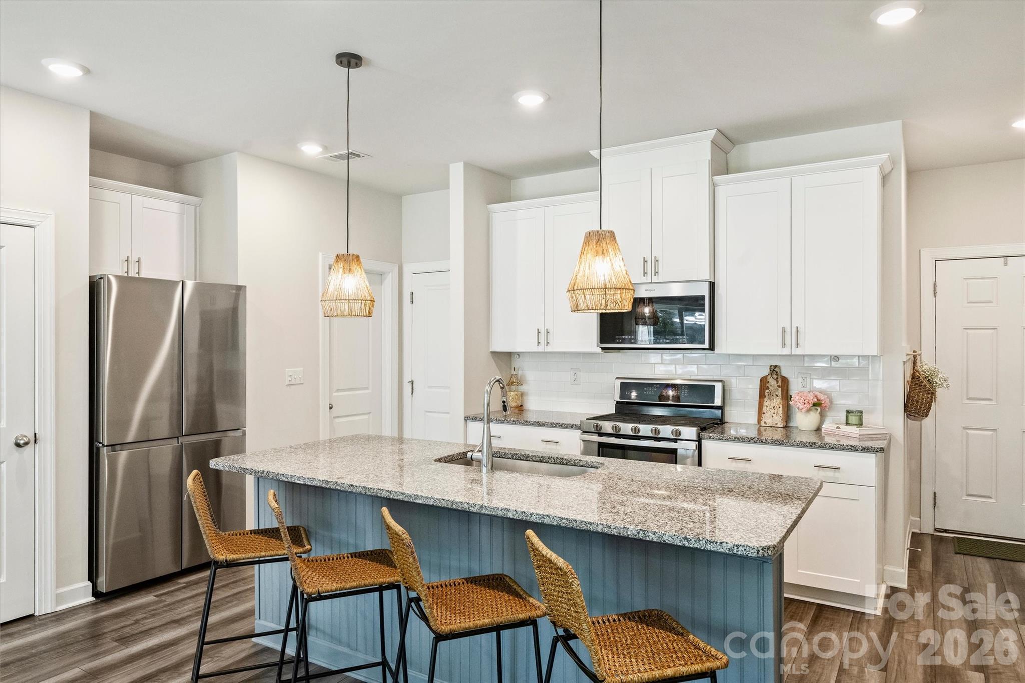Modern kitchen with a blue island, granite countertop, stainless steel appliances, and woven bar stools.