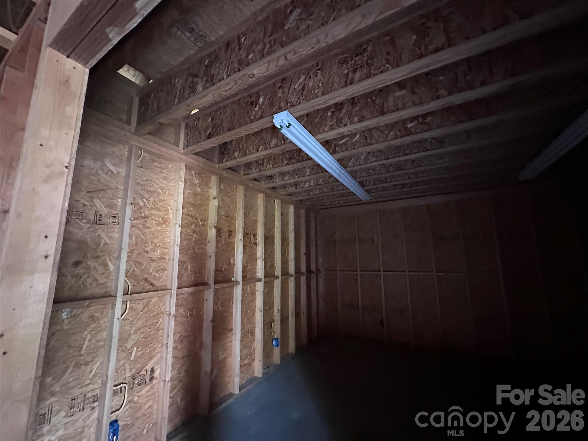 Unfinished garage with exposed wood framing, a concrete floor, and fluorescent ceiling lights.