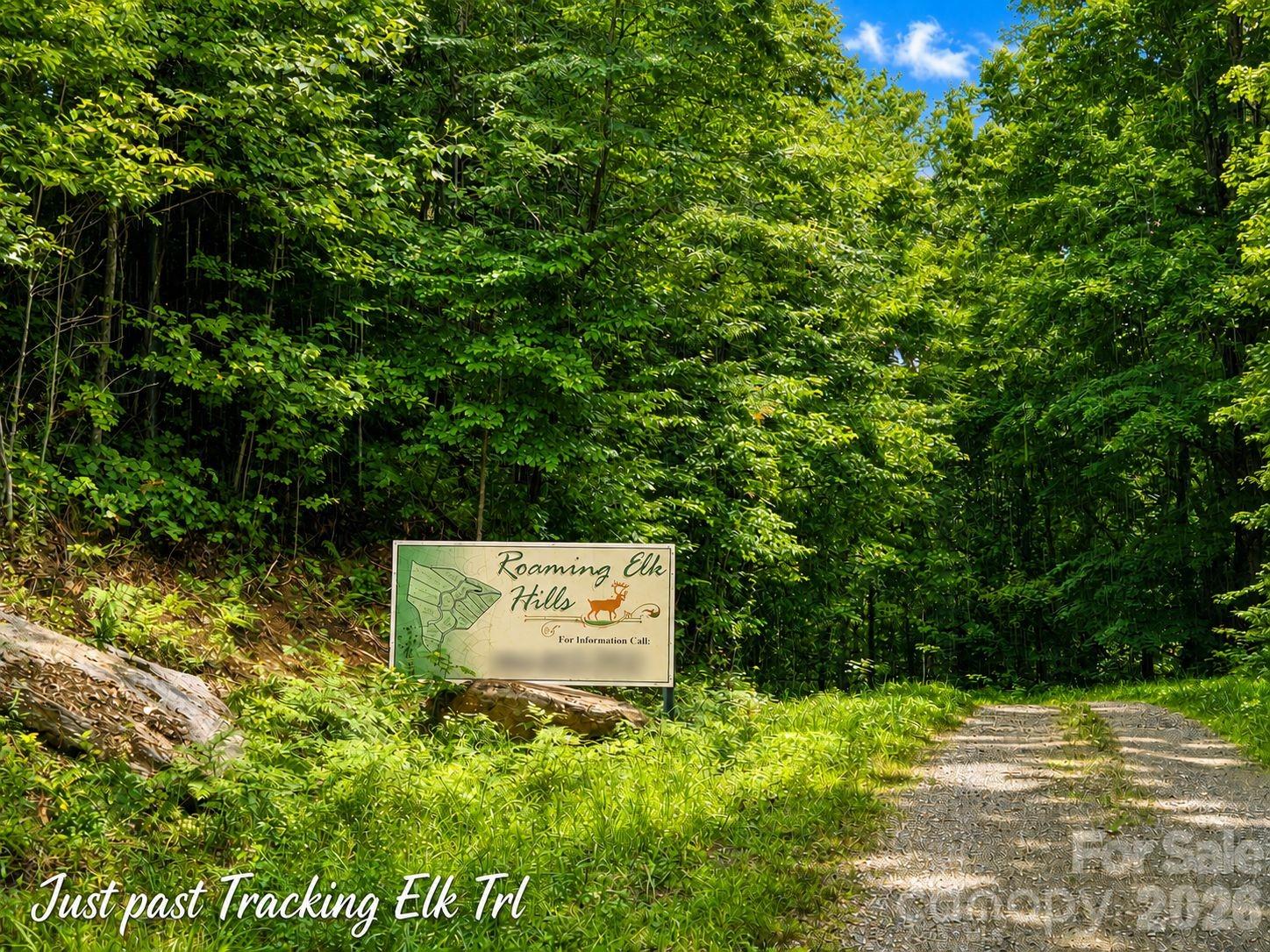 Gravel road through dense woods beside a Roaming Elk Hills development sign.