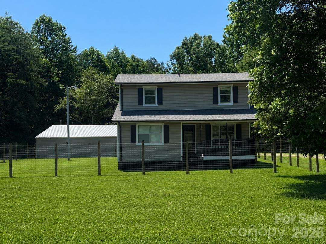 Two-story gray house with dark shutters behind a fenced lawn and detached outbuilding.