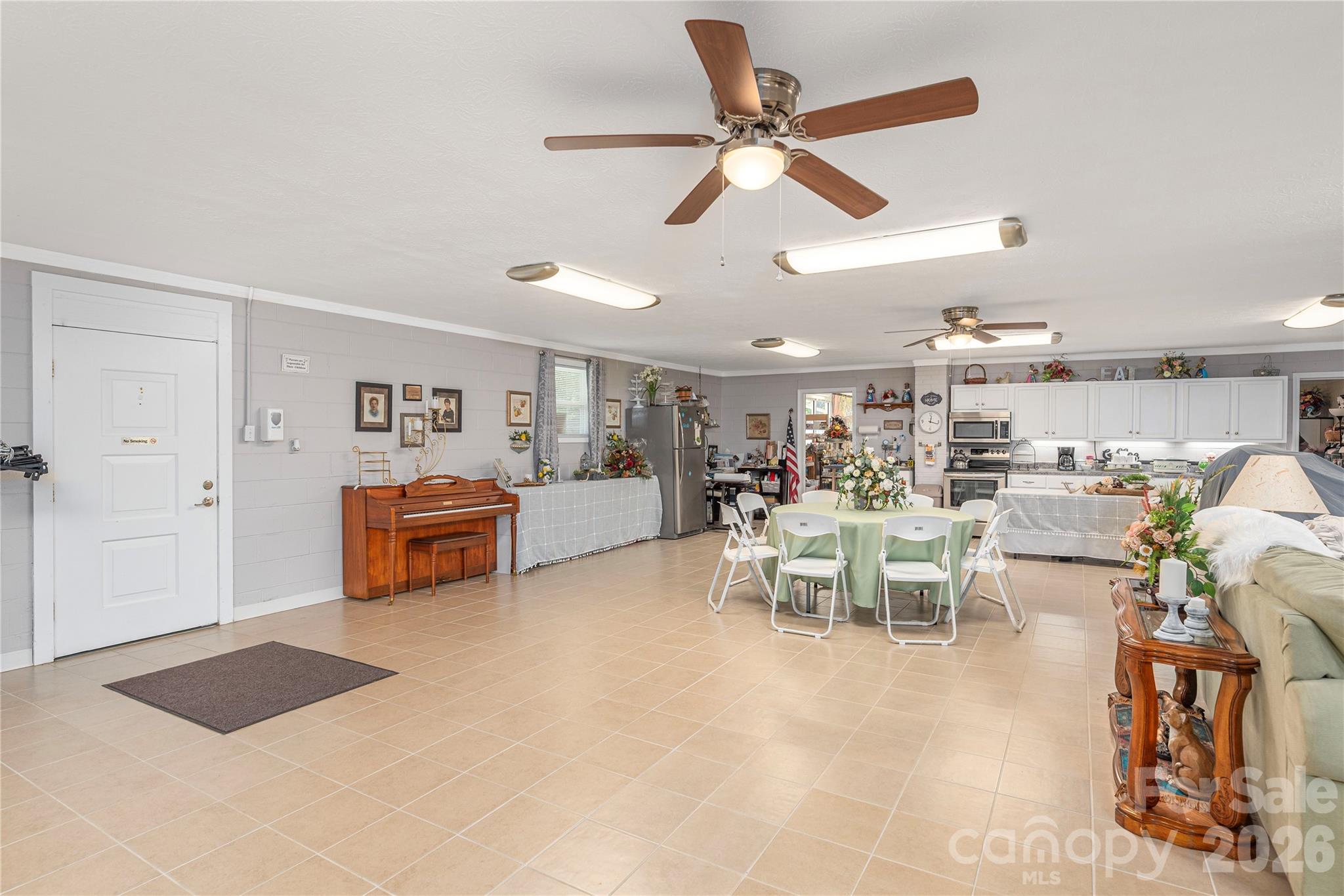 Open communal room with a dining table, kitchen cabinets, piano, and ceiling fans.