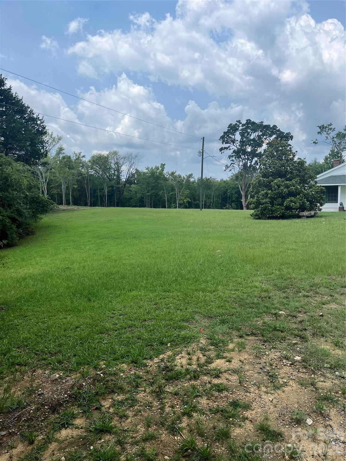 Grassy residential lot with a wooded edge and part of a house at the right.