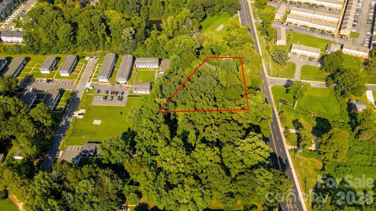 Aerial view of a wooded parcel outlined in red beside a road and apartment buildings.