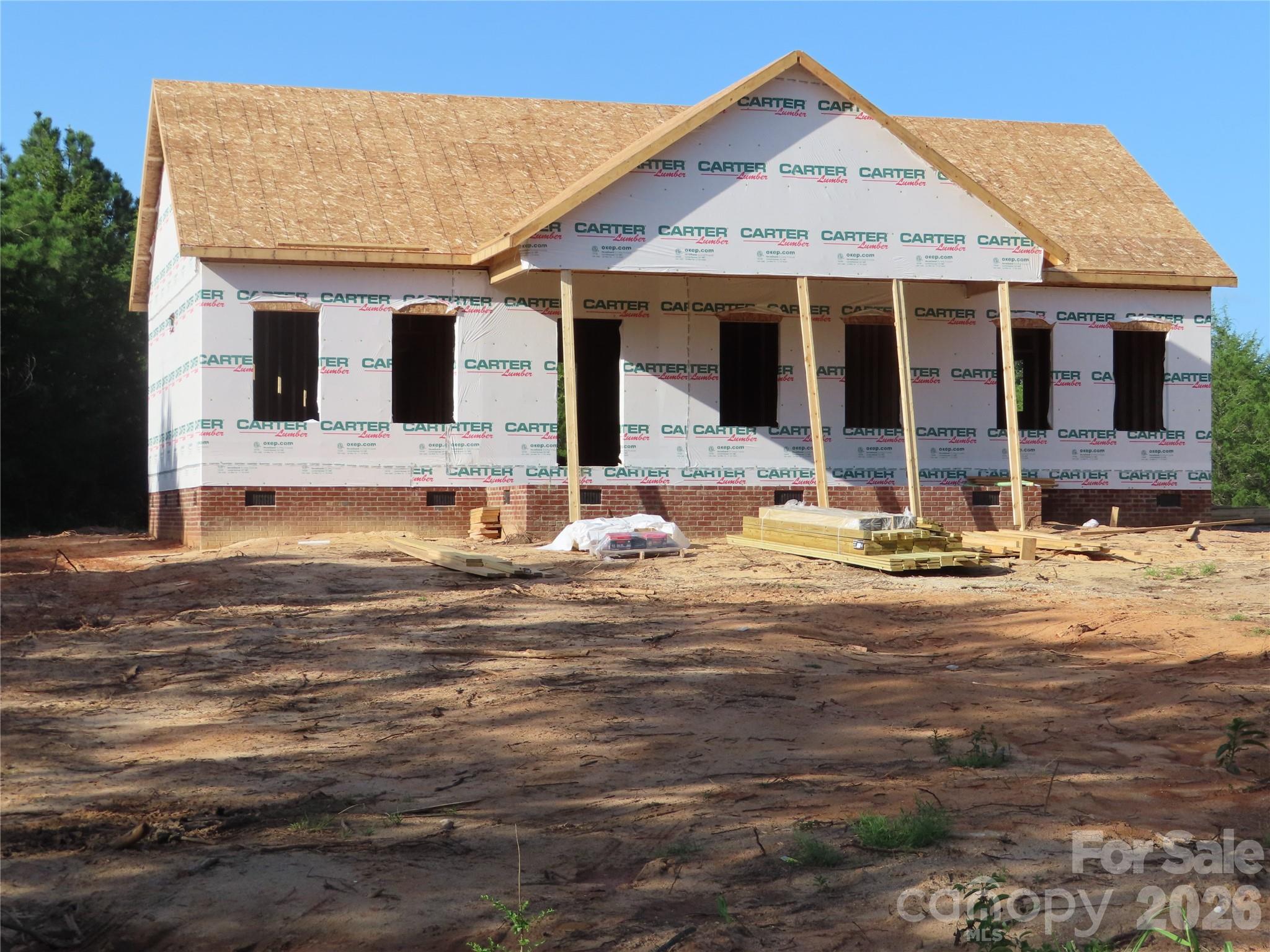 Two-story house under construction with exposed roof sheathing and house wrap.