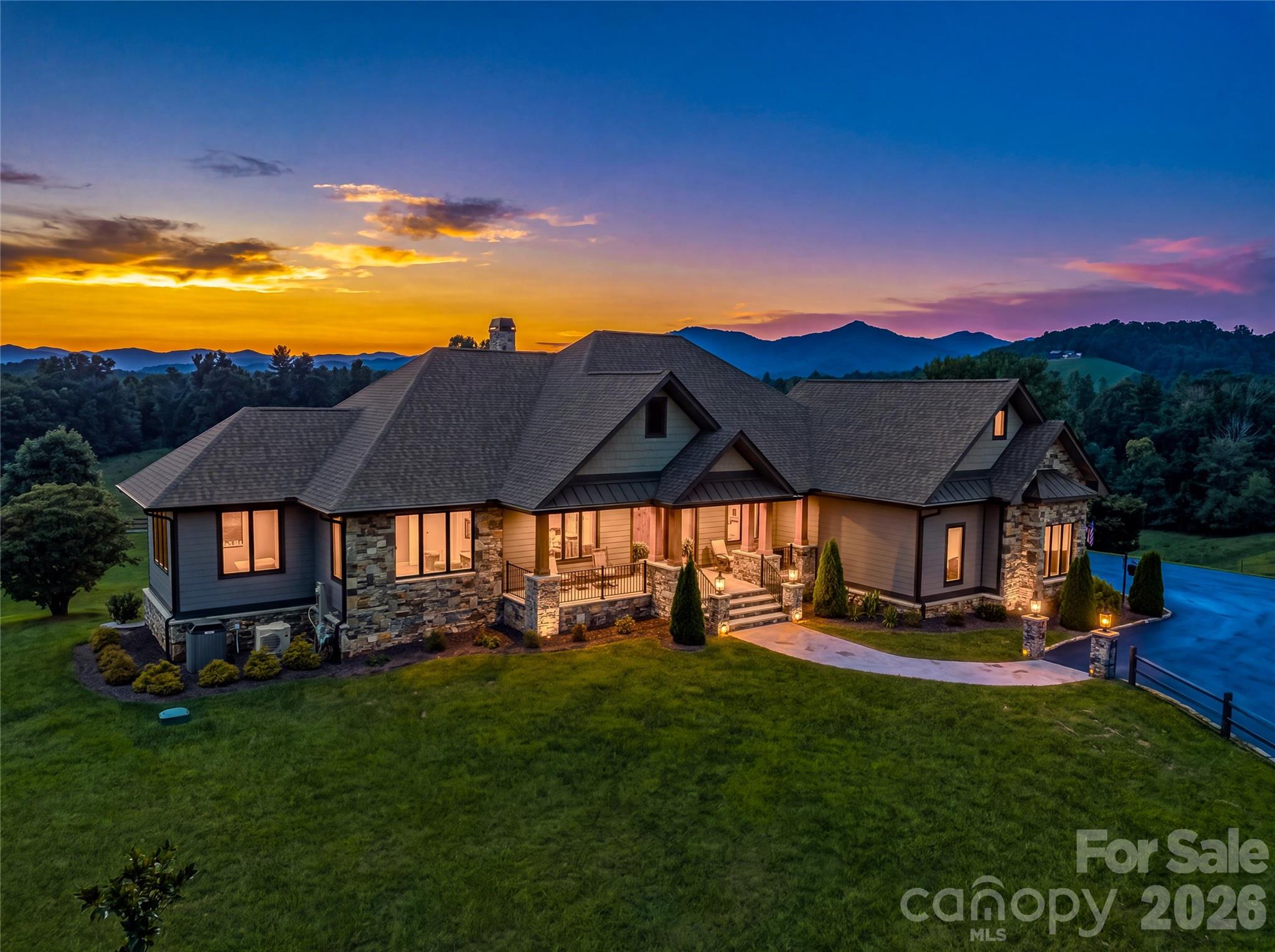 Large stone-accented home with a covered porch and pool, illuminated against a colorful dusk sky.